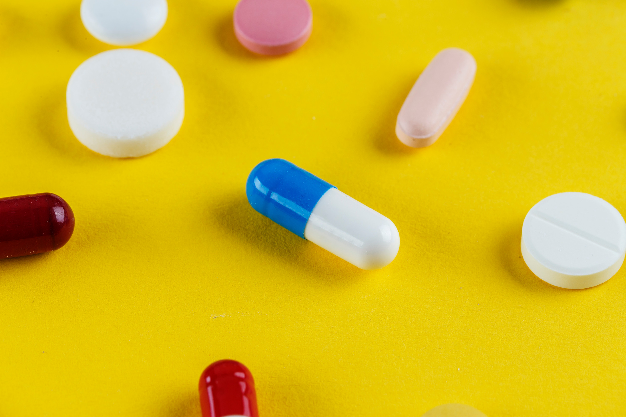 various pills and capsules scattered on a yellow background