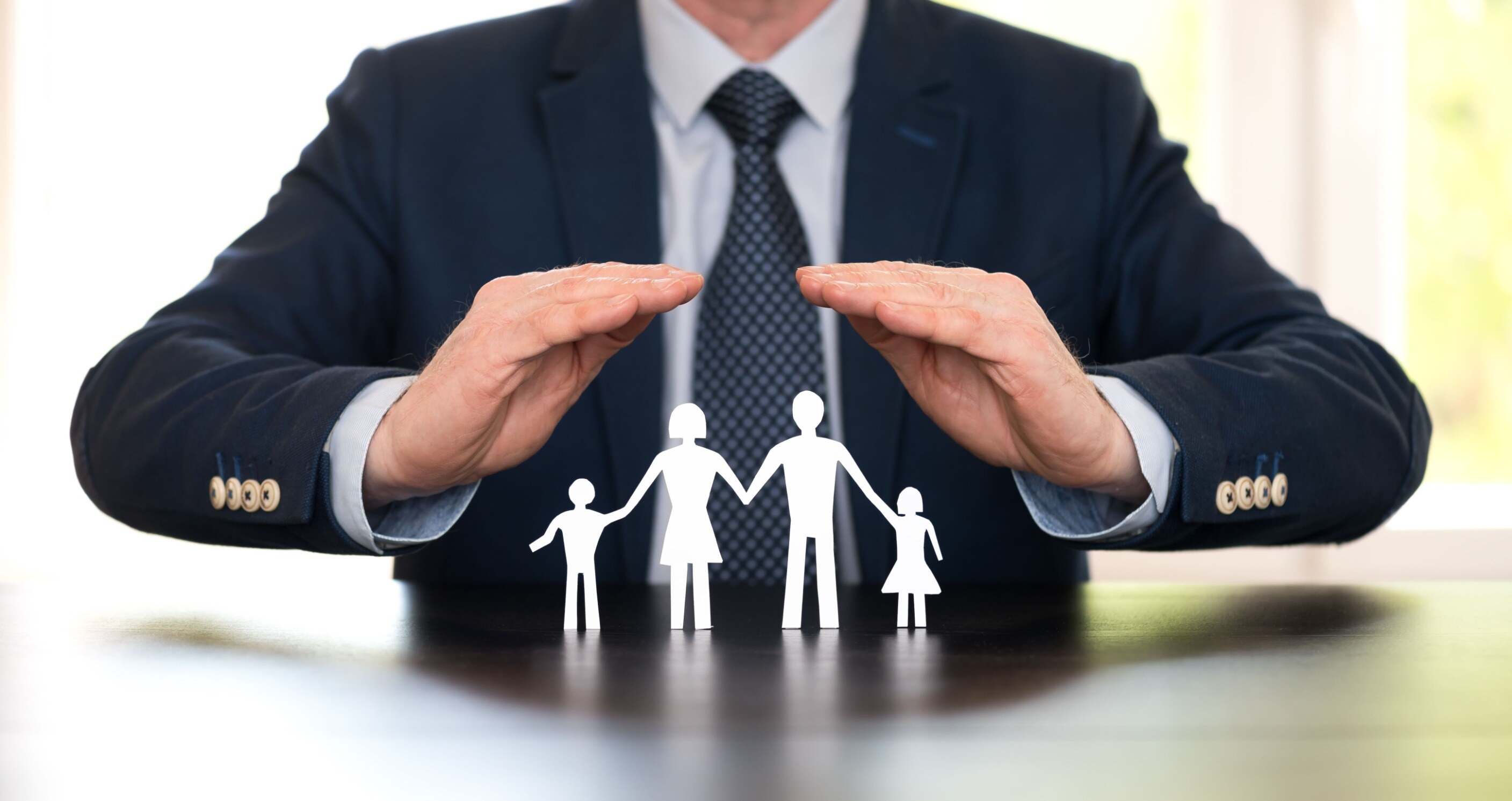 man in business attire holding his hands over paper cutout of a family