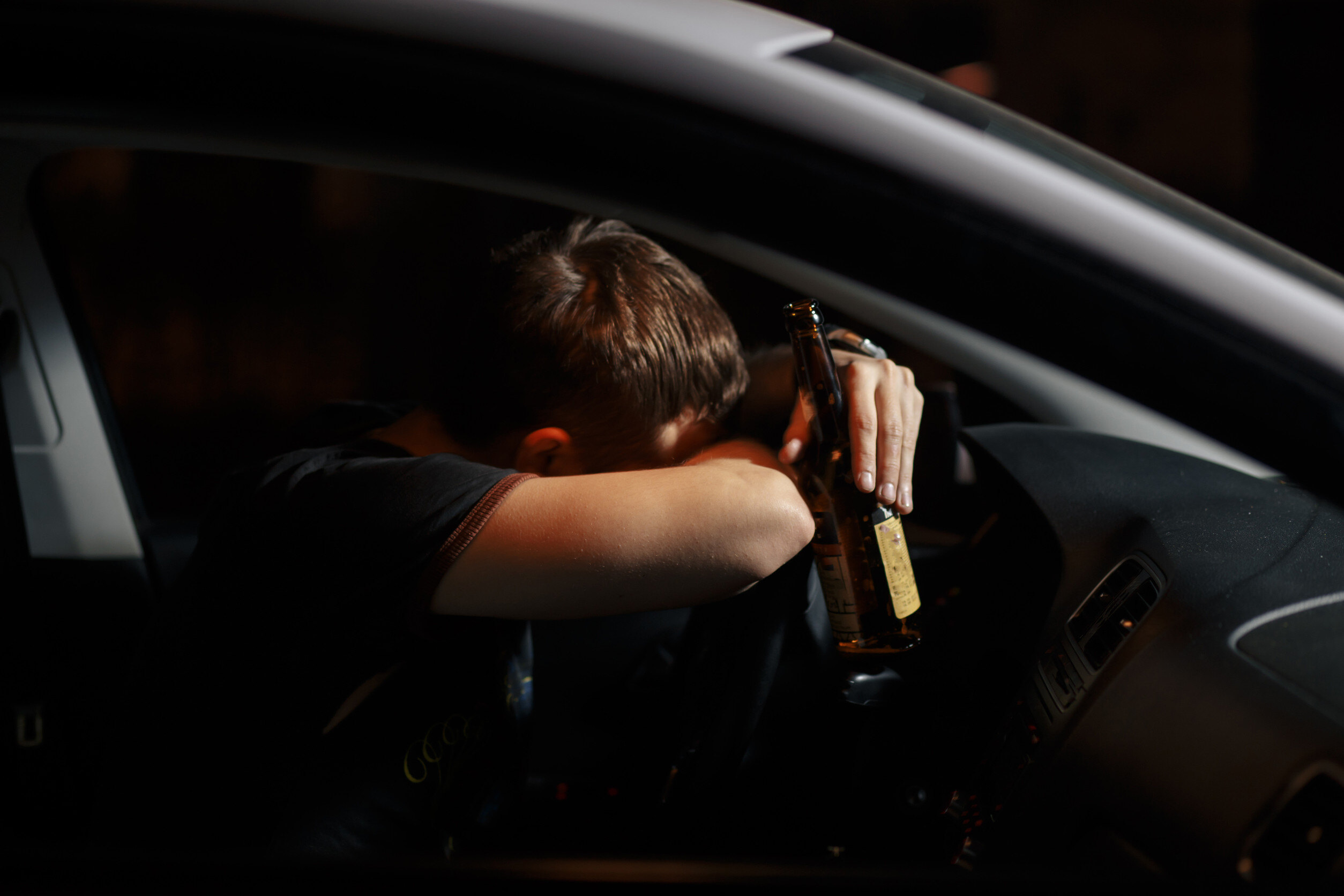 a man leans his head and arms against a steering wheel while holding a beer bottle in one hand