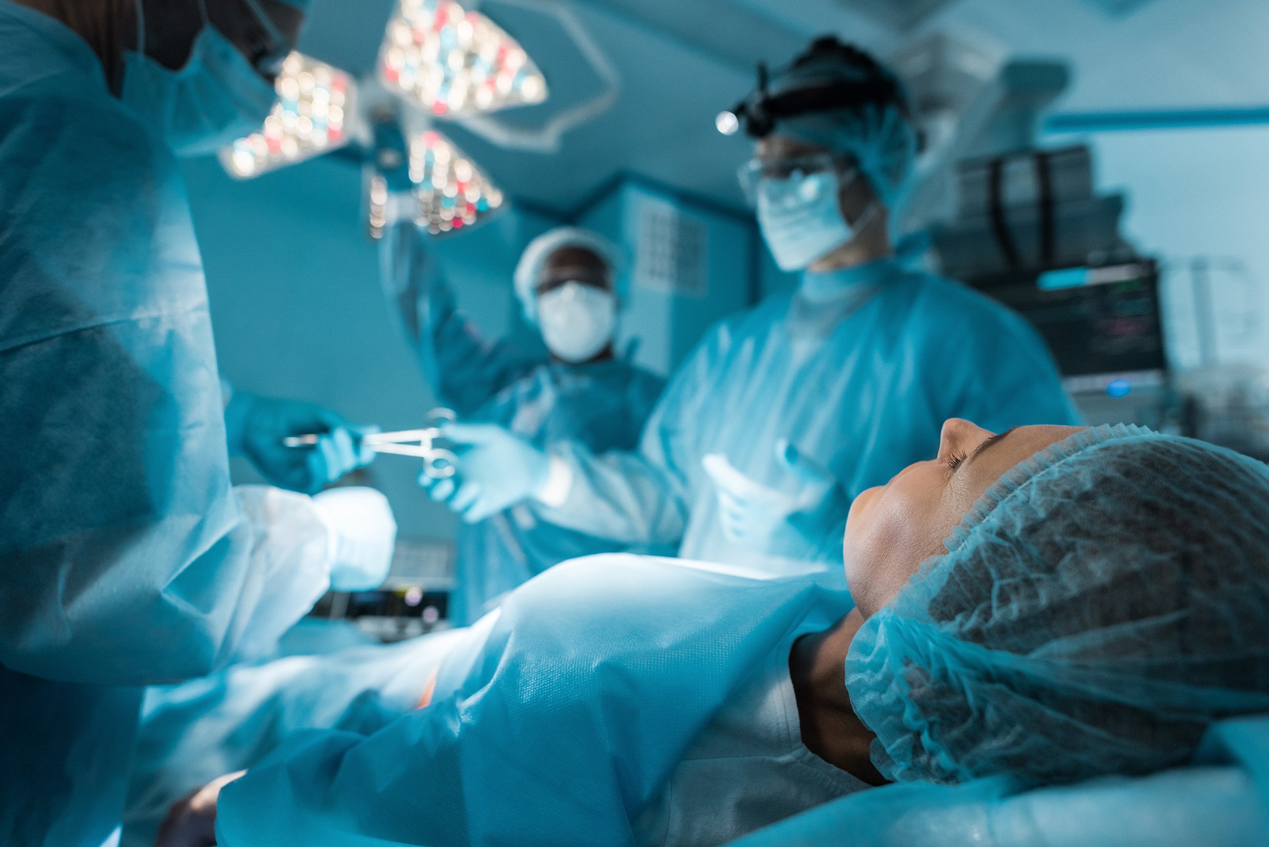 a woman lies on a bed in an operating room as a team of surgeons treat her