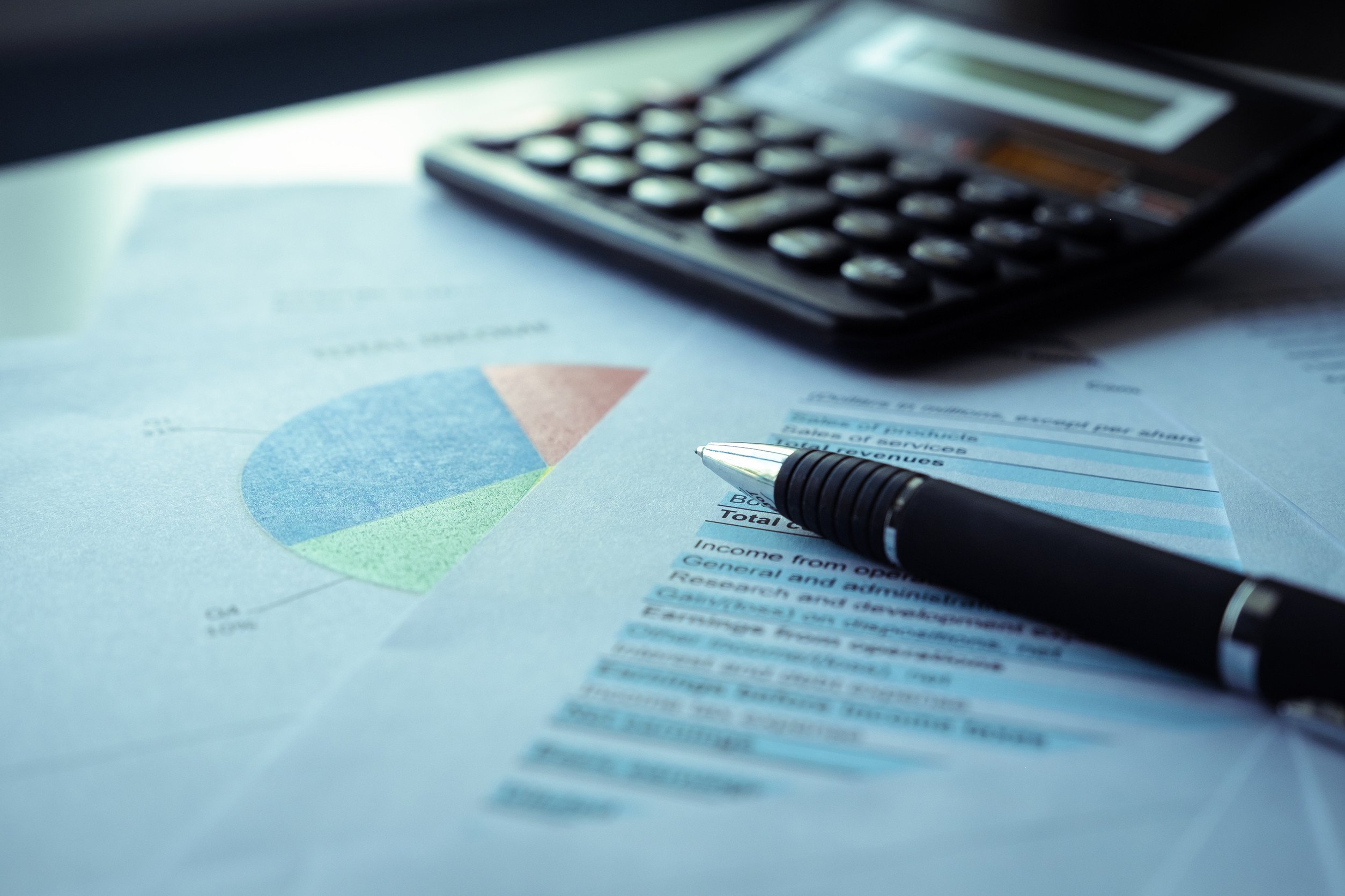 a pen and calculator lay atop a stack of financial documents on a desk