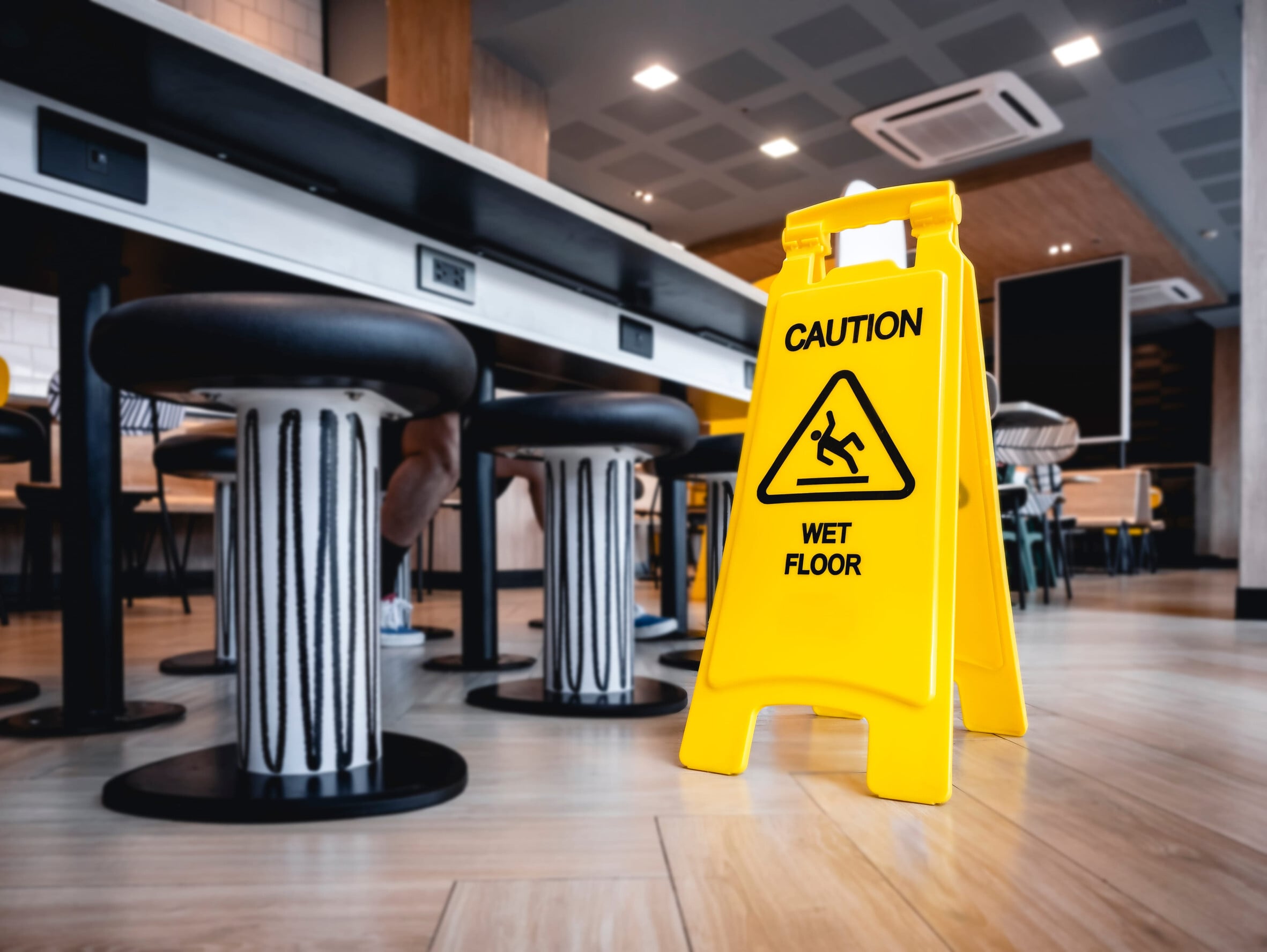 A bright yellow caution sign stands prominently in a modern café, alerting visitors to a wet floor