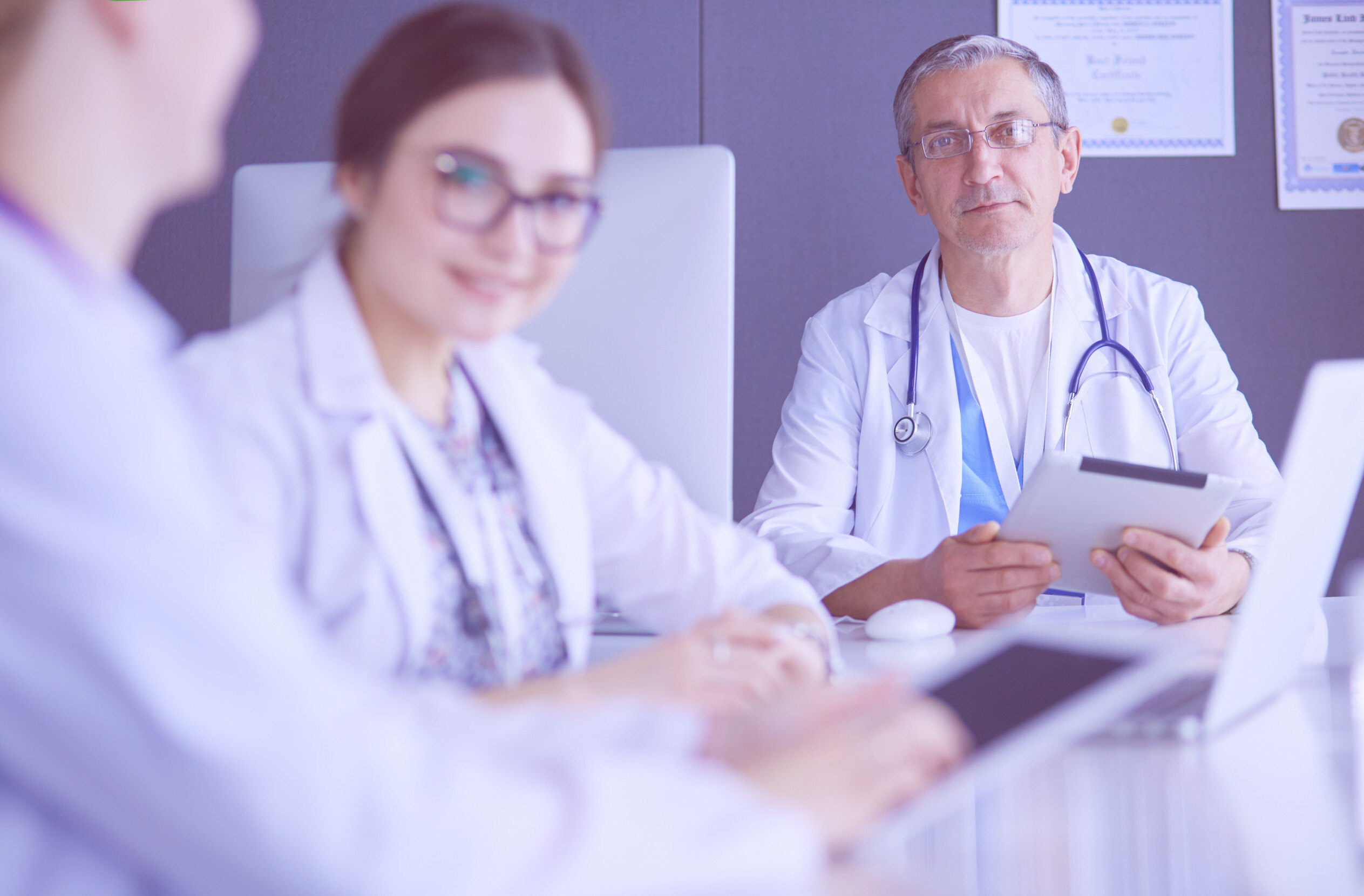 a group of doctors discussing medical matters while gathered around a table with laptops and tablets