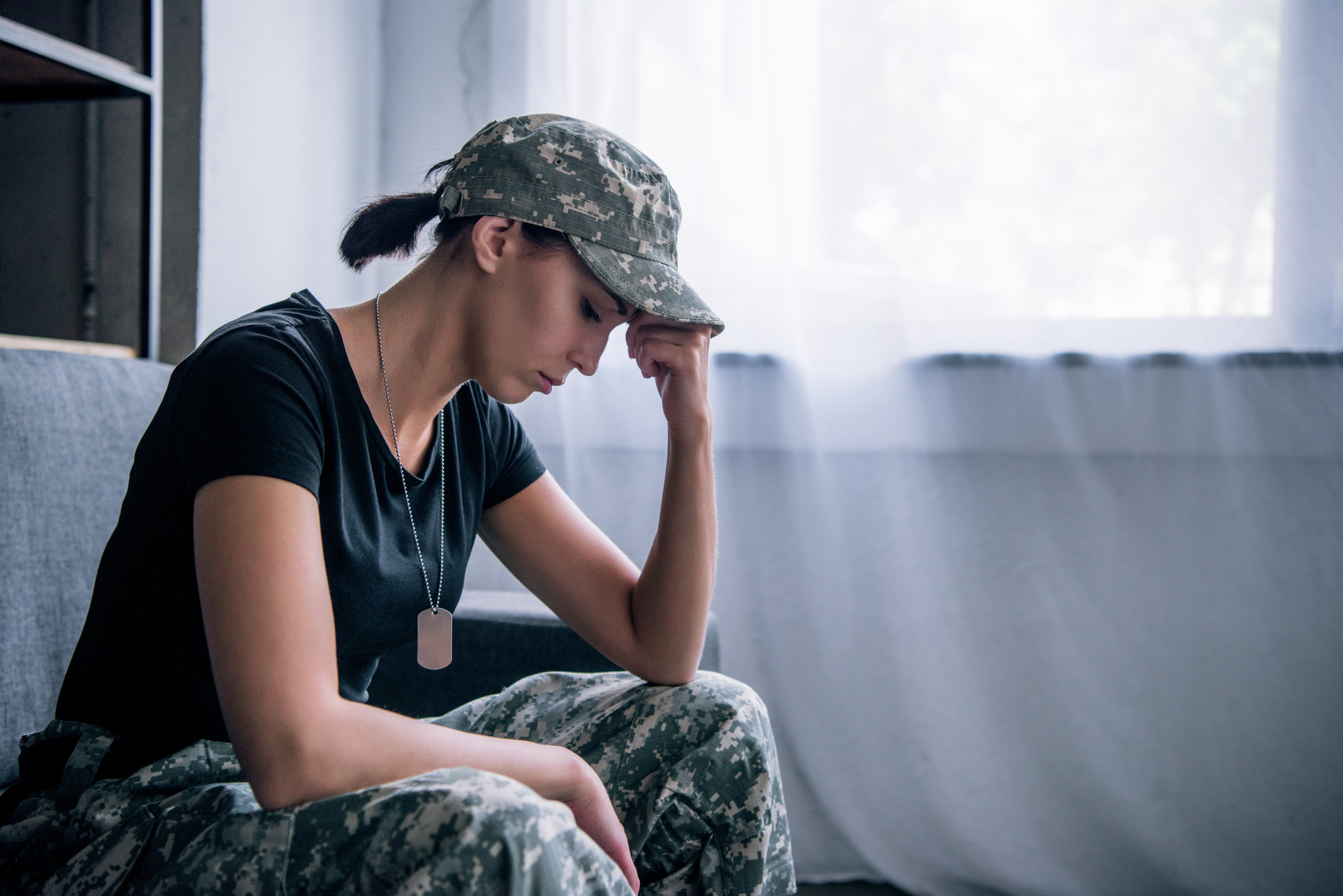 a soldier partially in uniform resting their head on their hand and appearing distressed