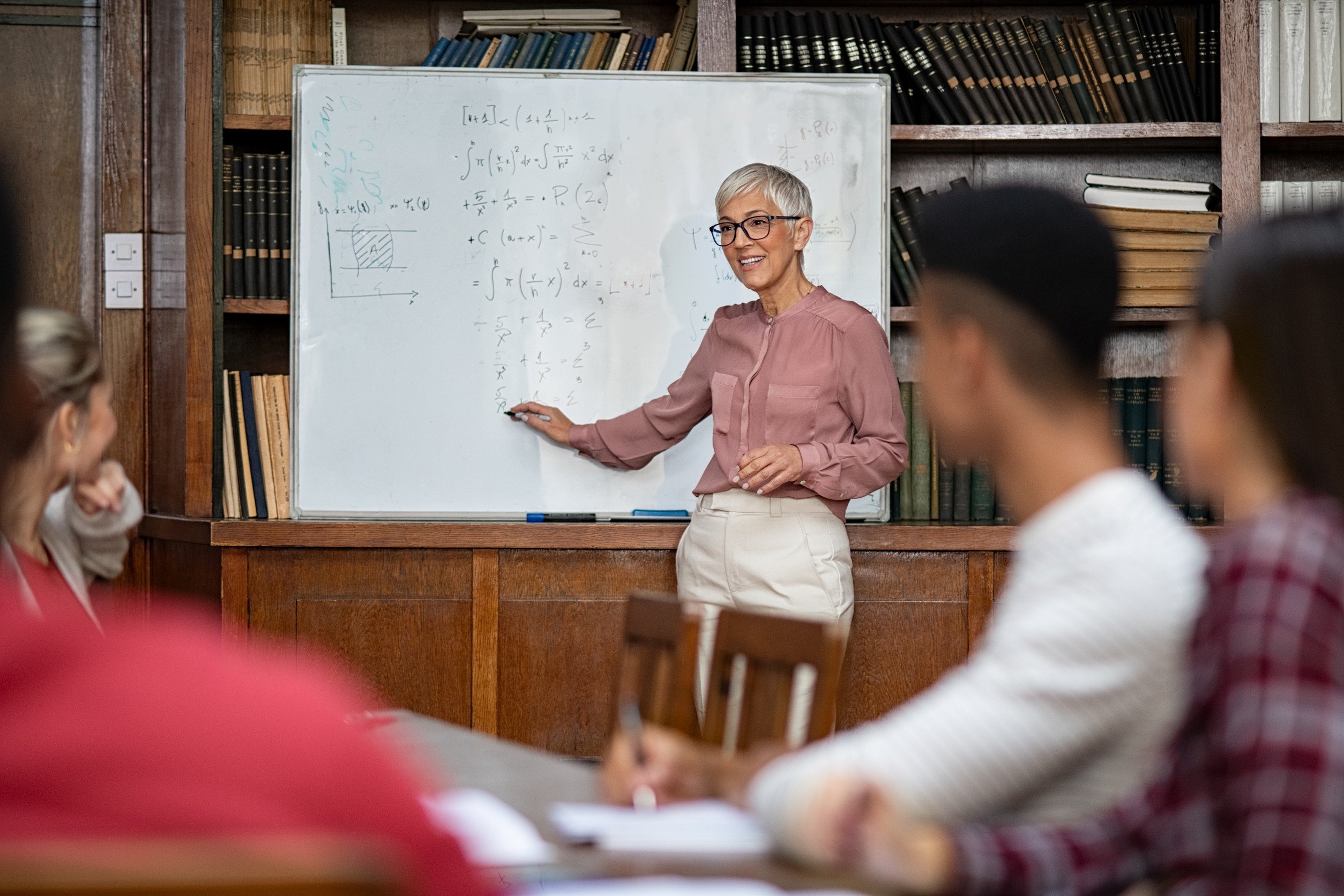 a college professors standing in front of a whiteboard explaining mathematical concepts to students