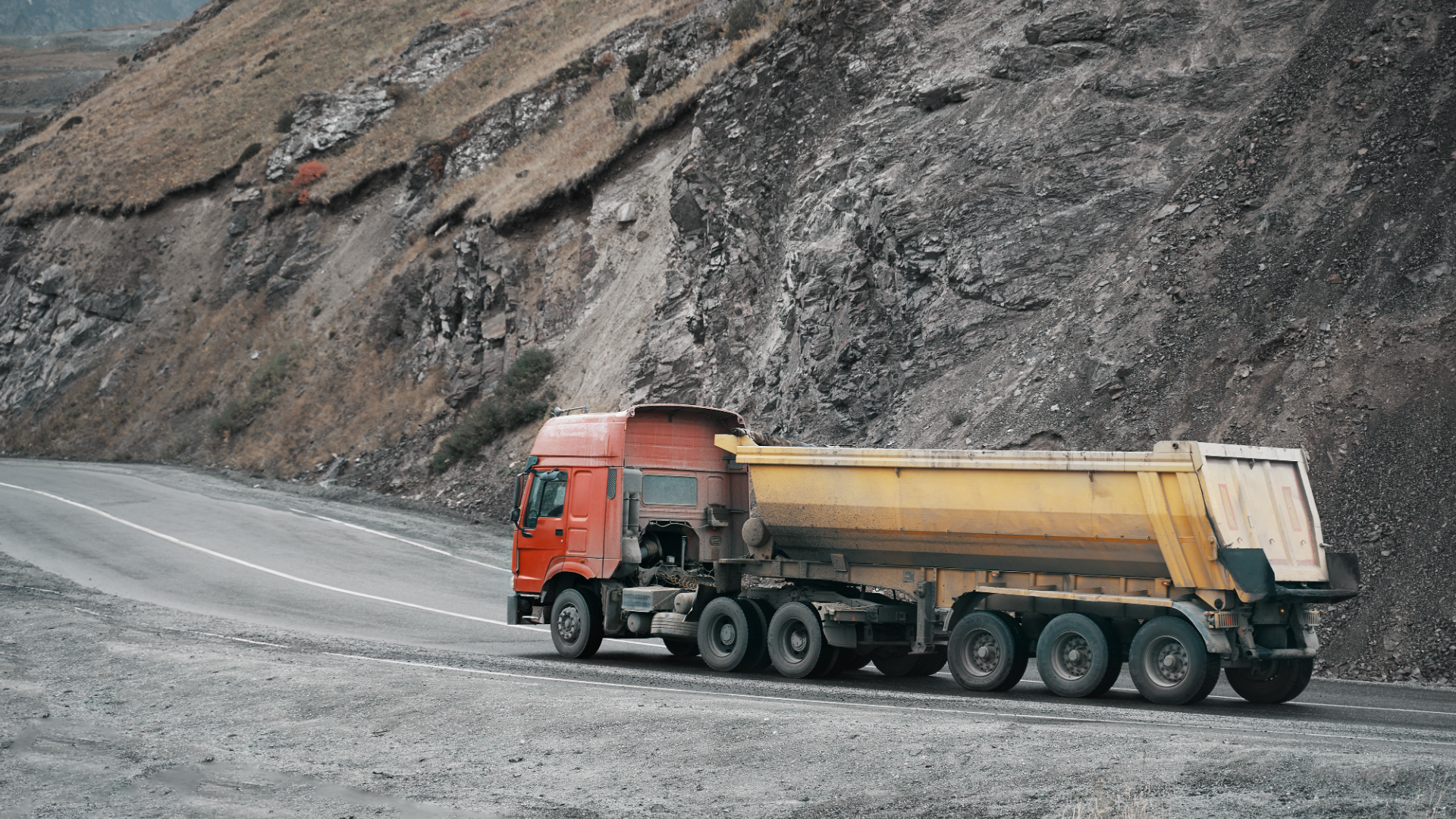 large diesel truck pulling a yellow trailer on road near a large hill