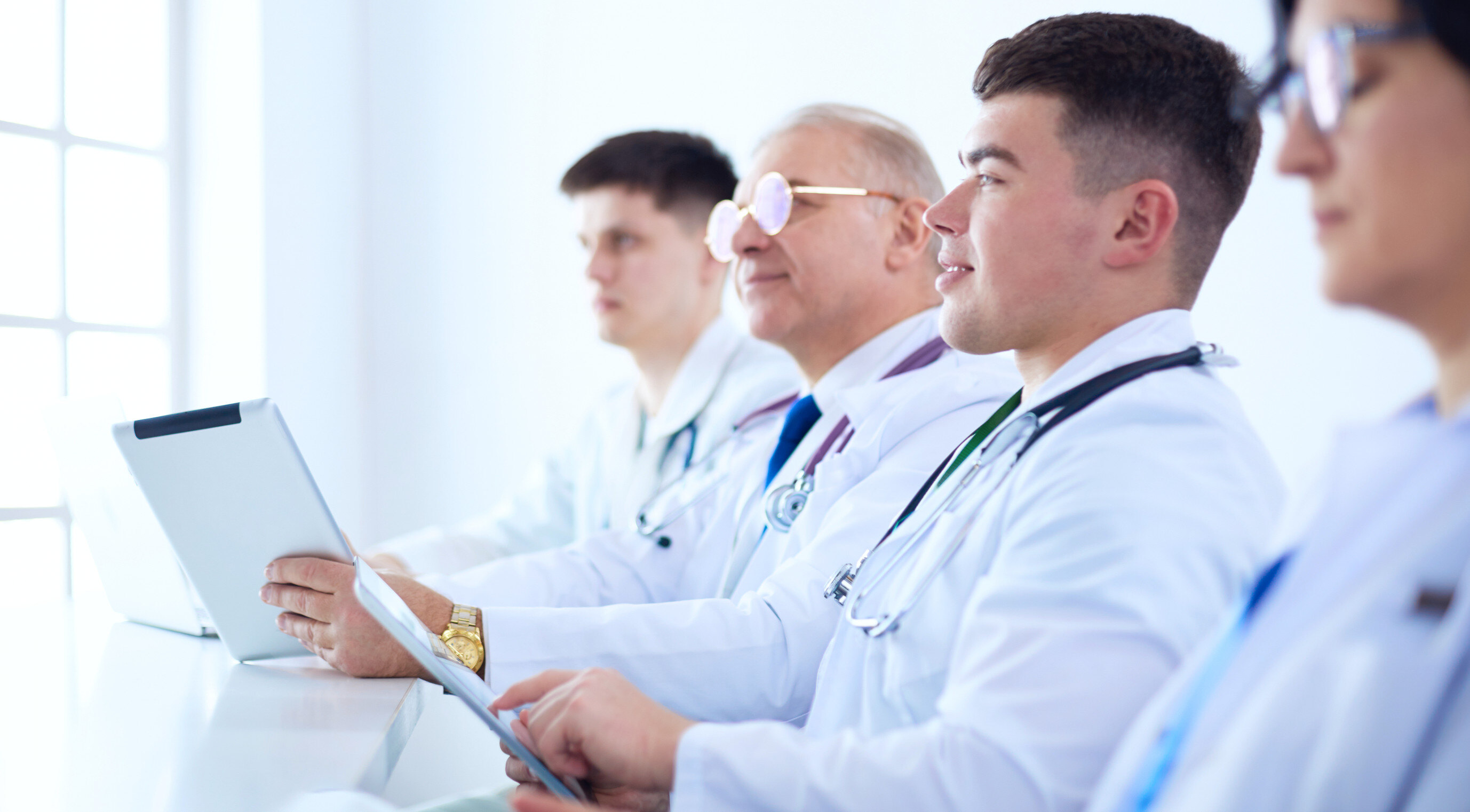 a panel of doctors in white coats sitting at a table holding tablets