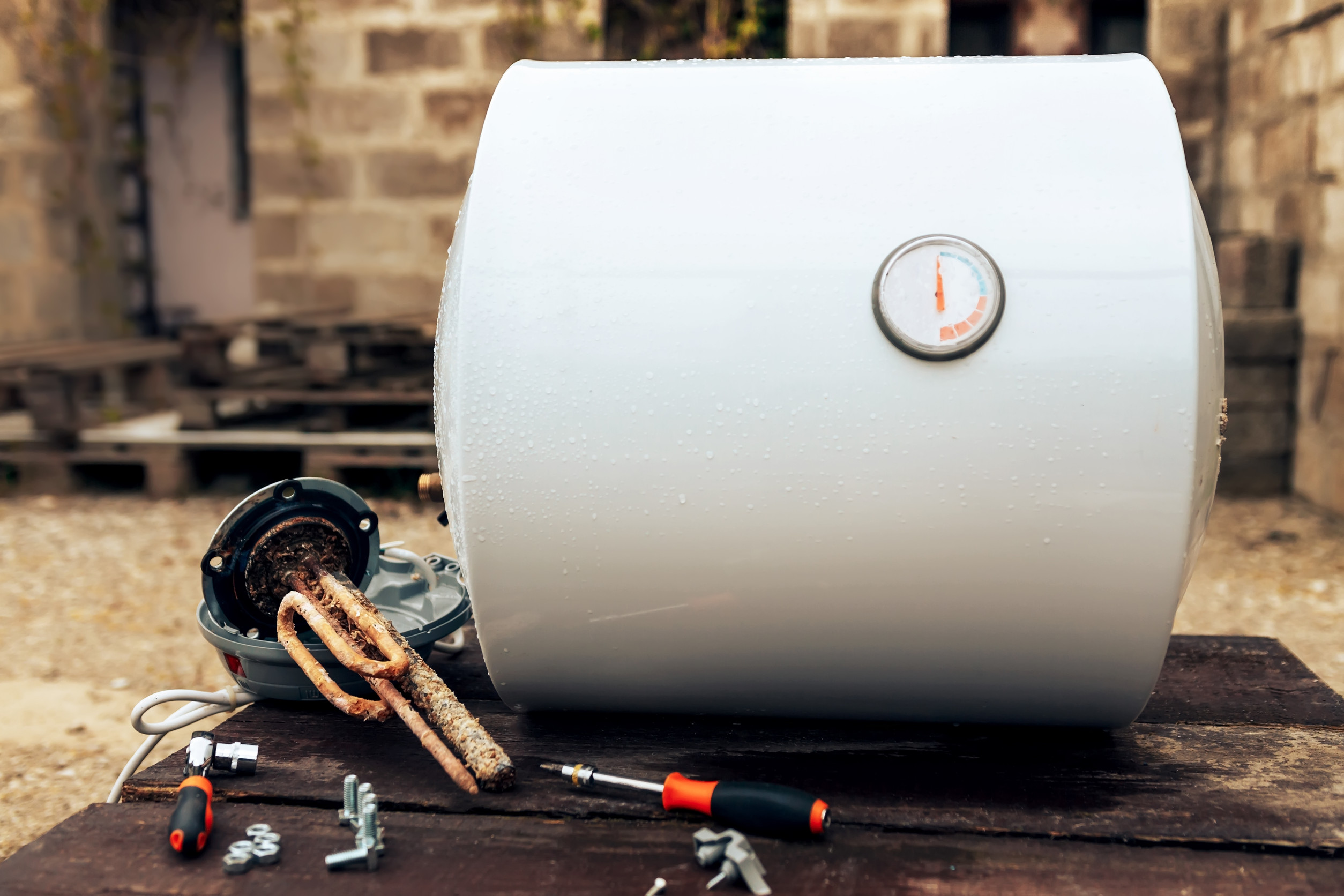 boiler disassembled, lying next to the heating element, nuts and tools on wooden surface, outside