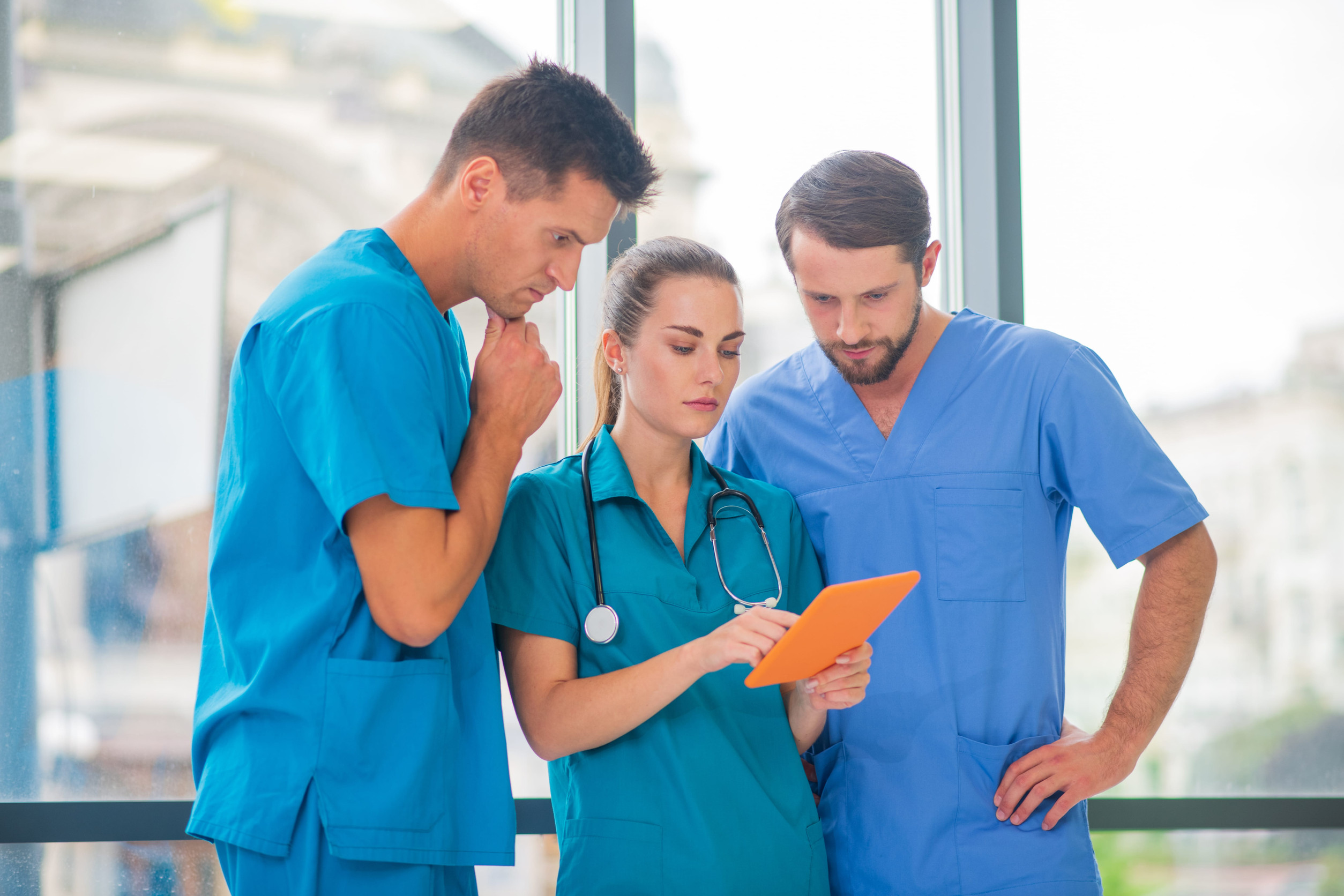 group of doctors and nurses gather around one tablet as they study it intently