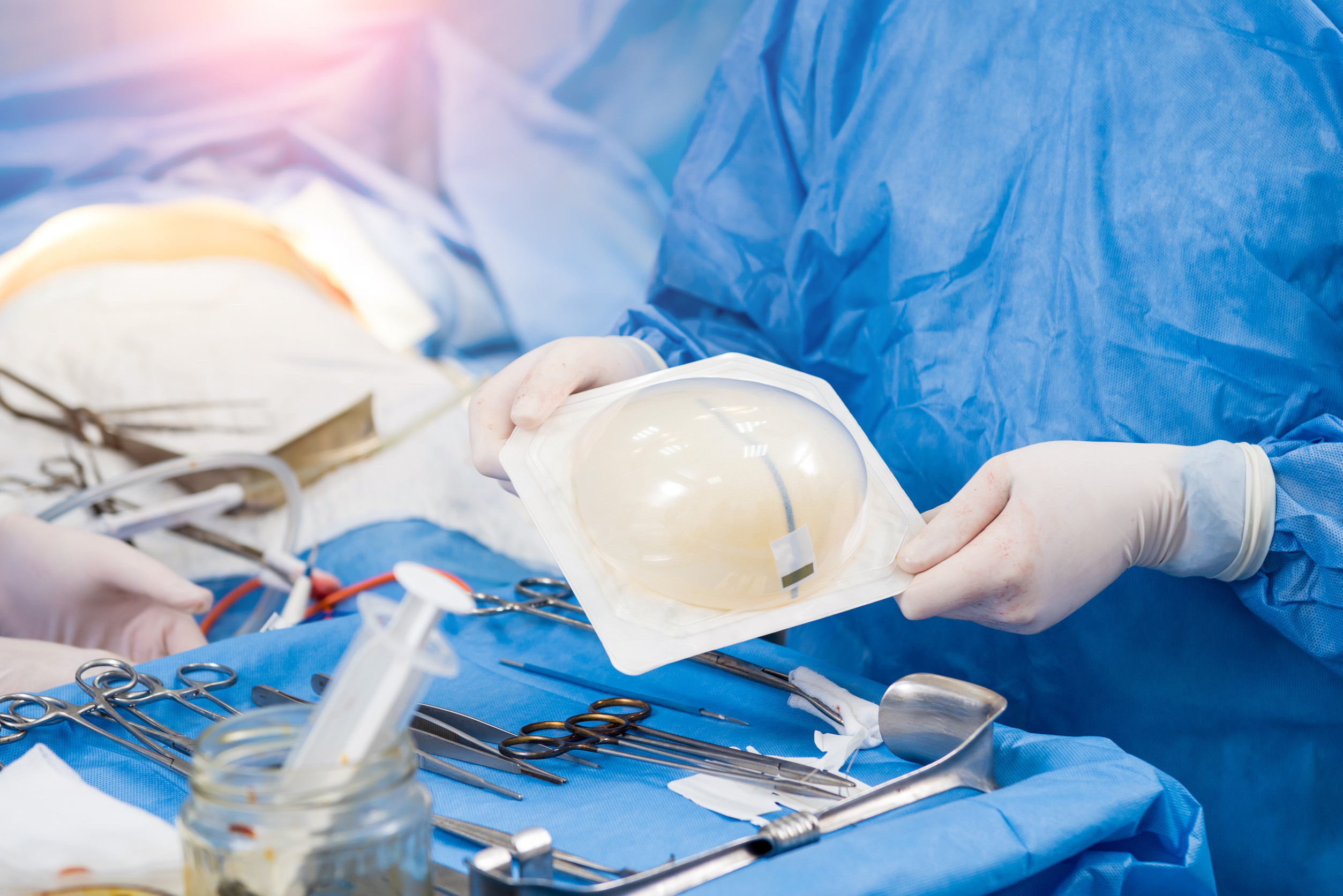 Surgeon in operation room is holding sterile breast silicone implant in hands