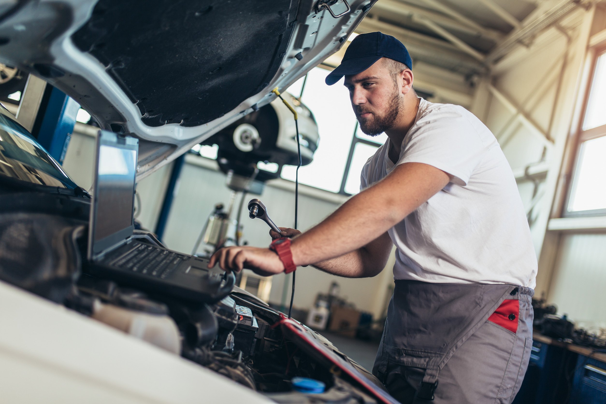 Professional car mechanic working in auto repair service using laptop