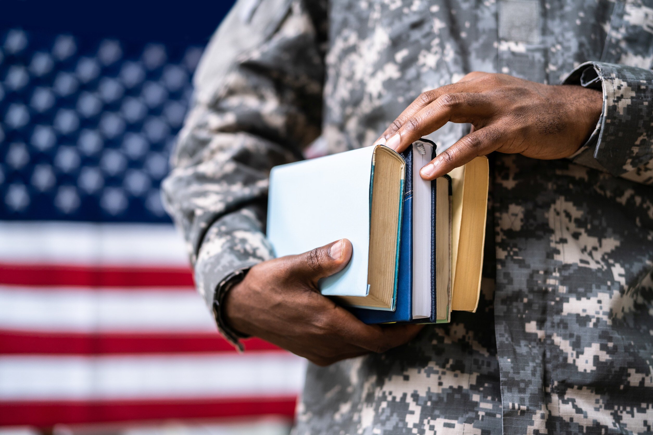 veteran in uniform holding books in front of a large american flag