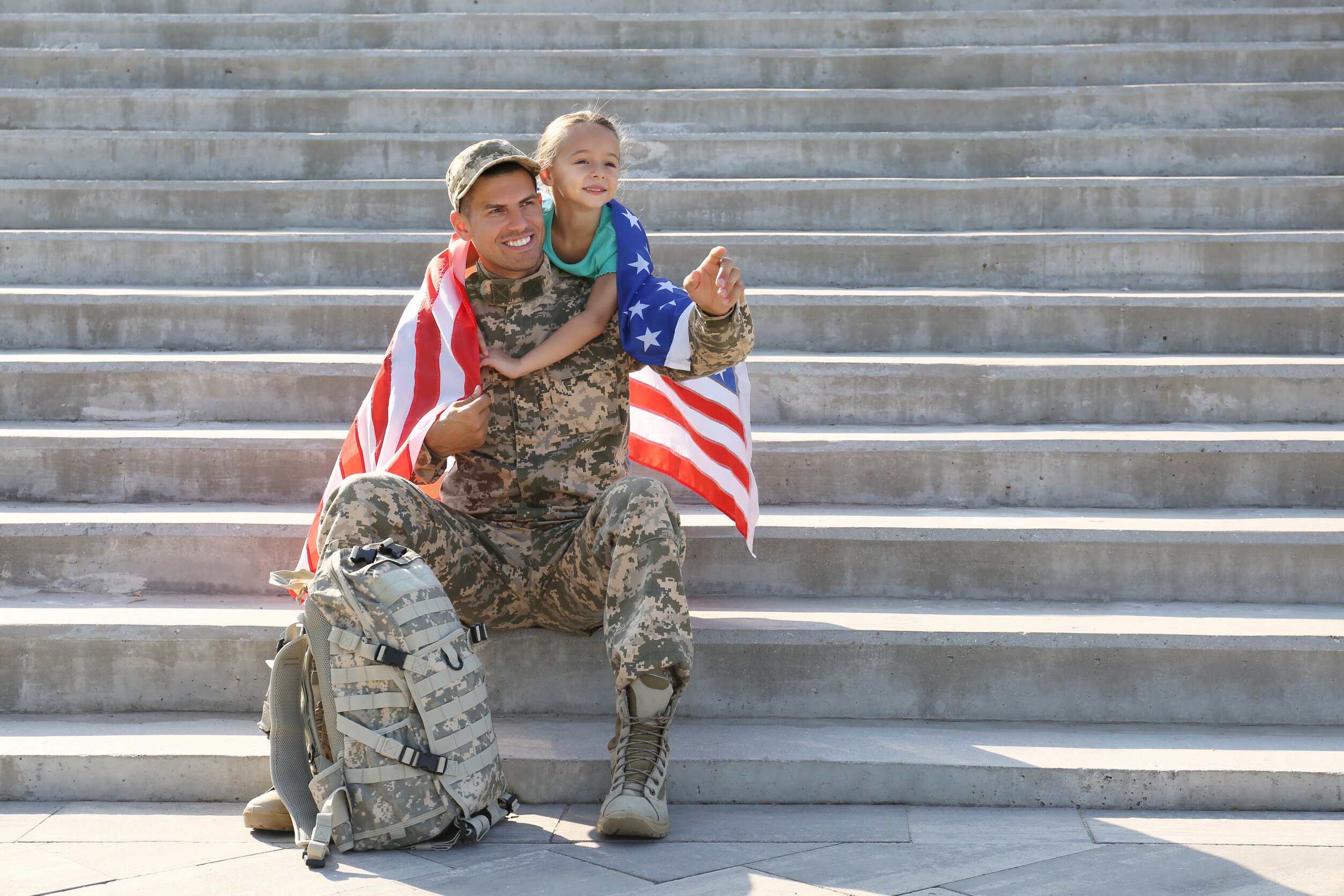 an american soldier and his child siting on concrete steps and wrapped in an american flag