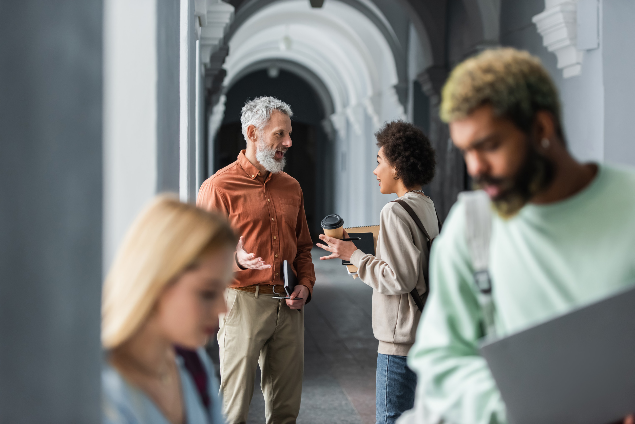 a professor and several university students socializing in a campus corridor