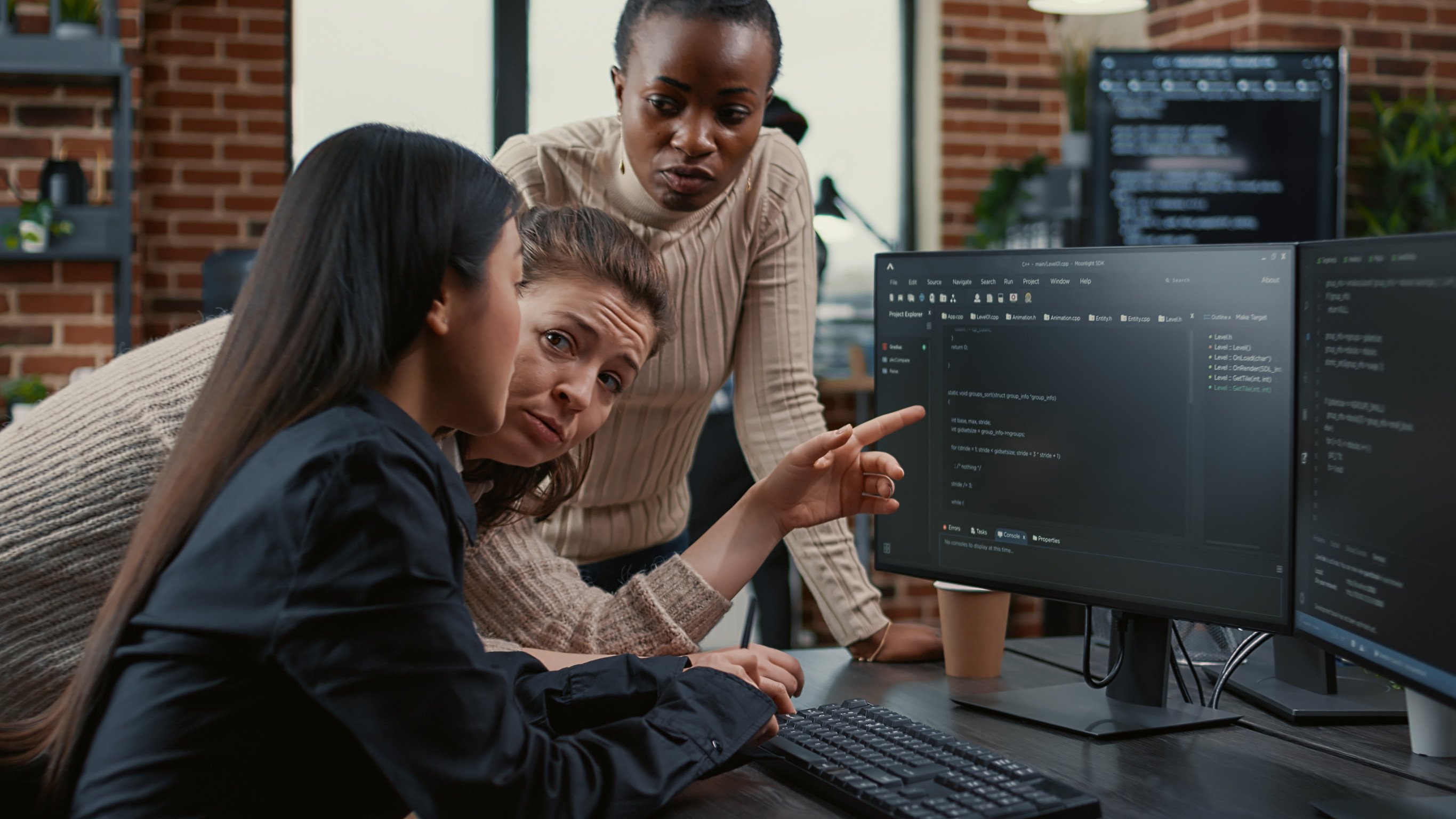 Programer pointing at computer screen explaining running code to coworkers