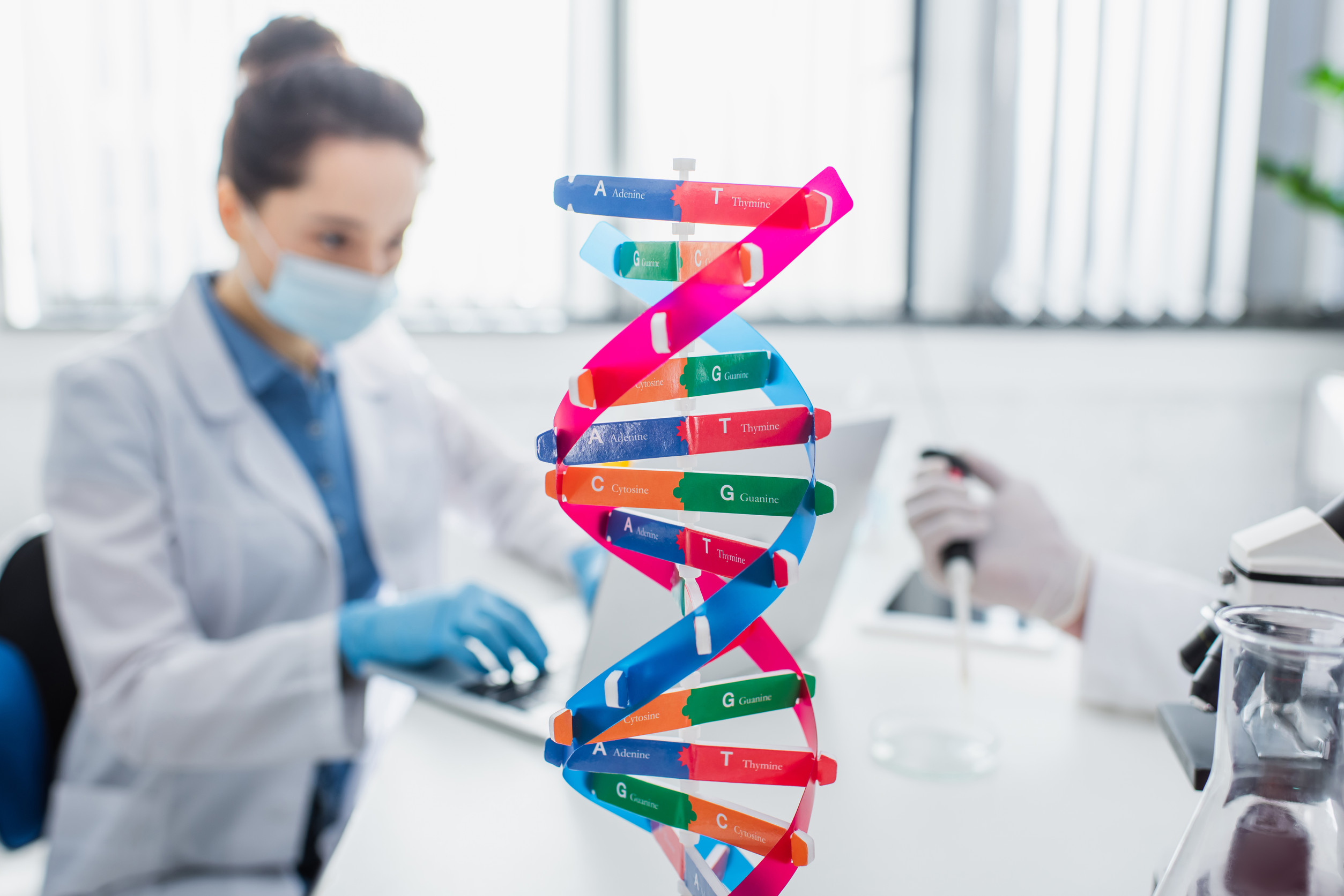 a large model of the double helix structure of DNA in focus in the foreground, with masked geneticists defocused in the background
