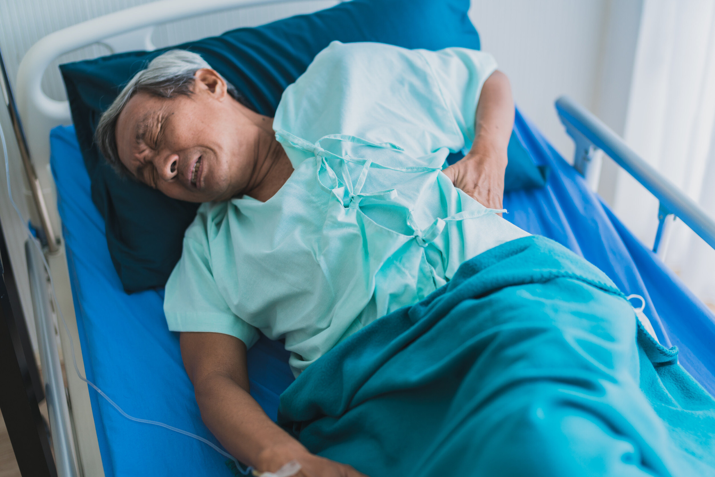 man in a hospital bed holding his side while making a pained expression