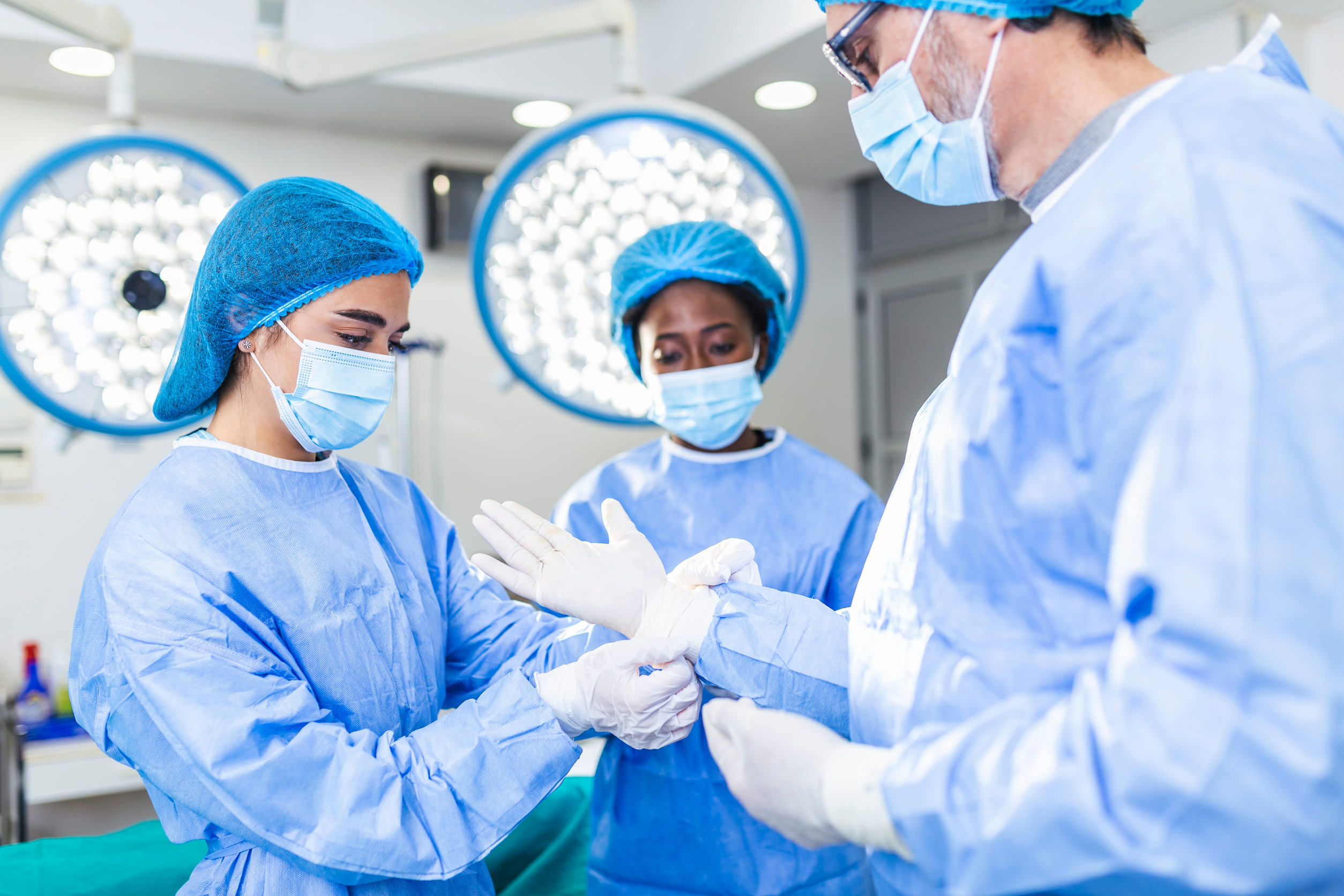 three medical professionals preparing for surgery by putting on protective gear