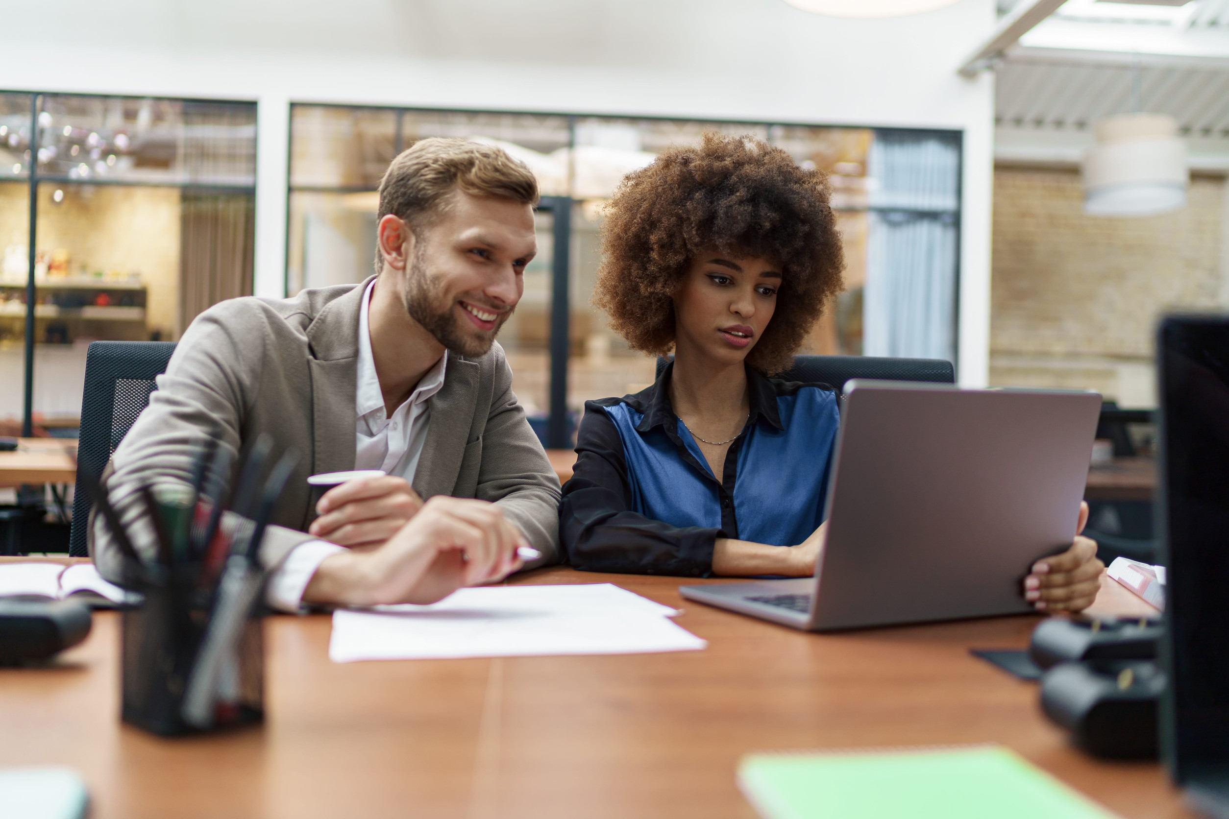 two office workers share a desk and look at the same laptop together