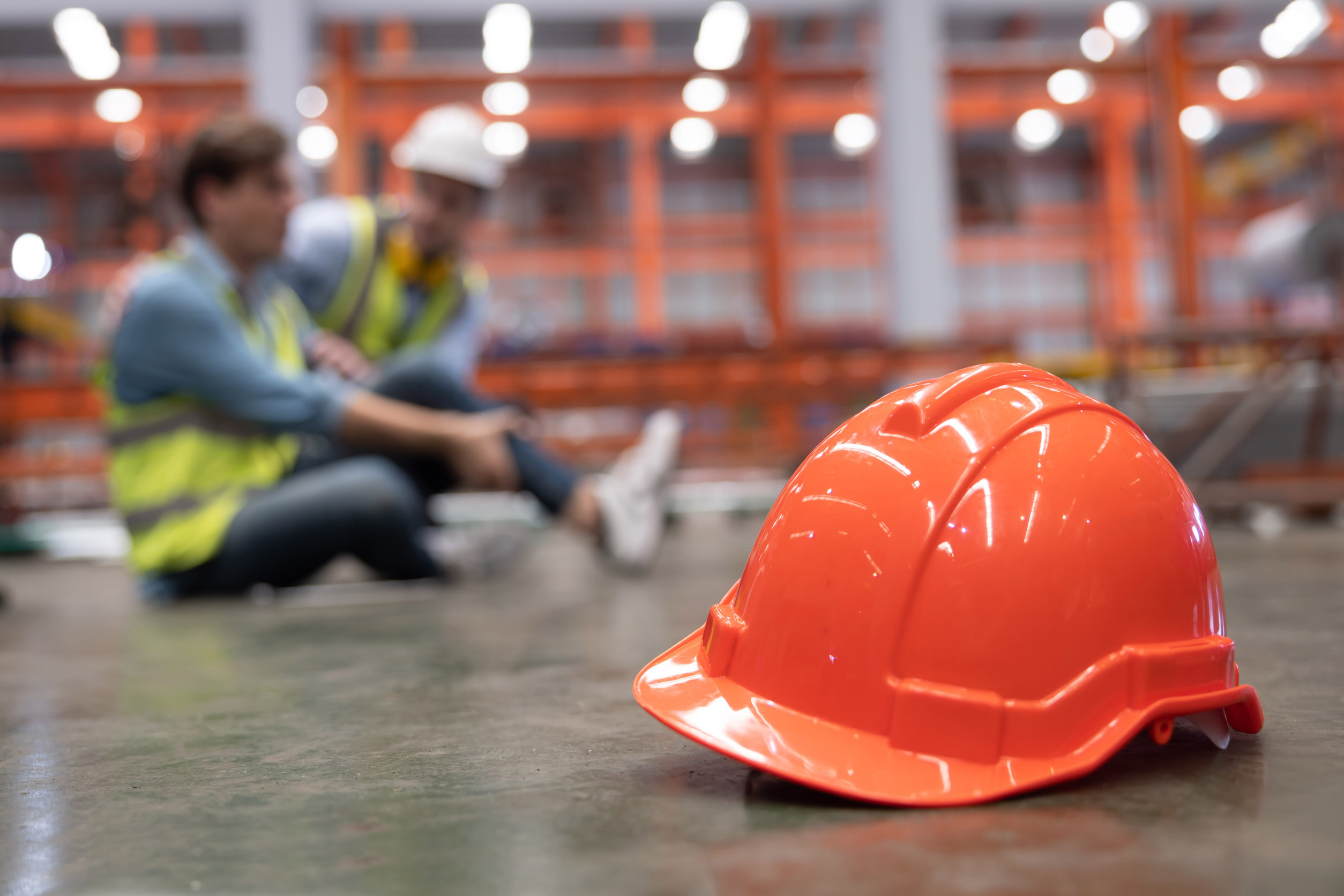 Close Up on Red Hard Hat with Blurred Injured Factory Workers as a Background