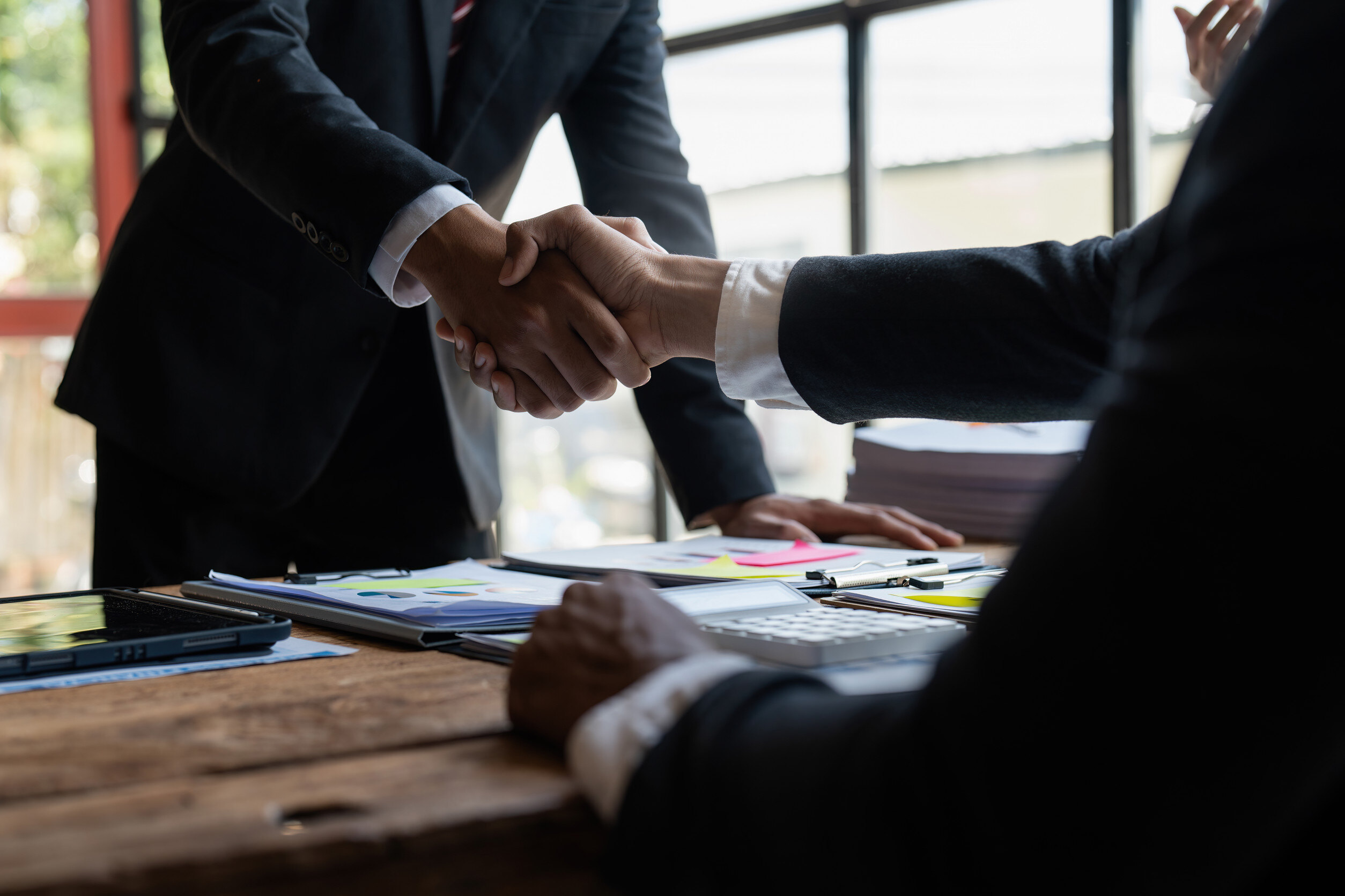 two business professionals shake hands over a desk
