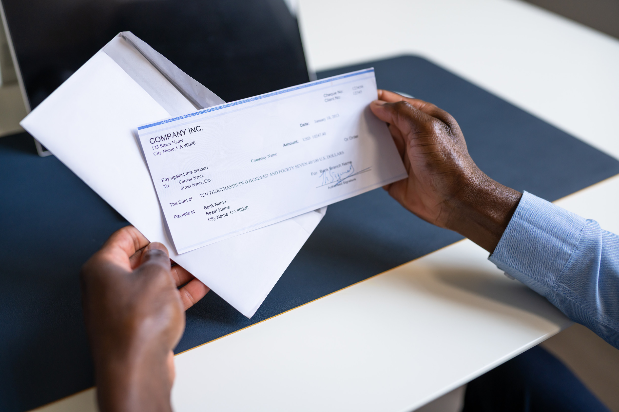 photo of a person's hands holding a payroll check pulled from an envelope over a desk
