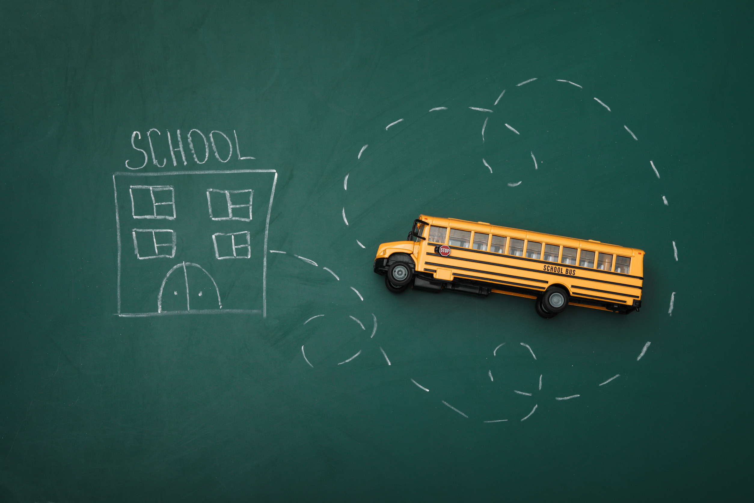a toy school bus rests on a chalk board with a drawing of a schoolhouse on it