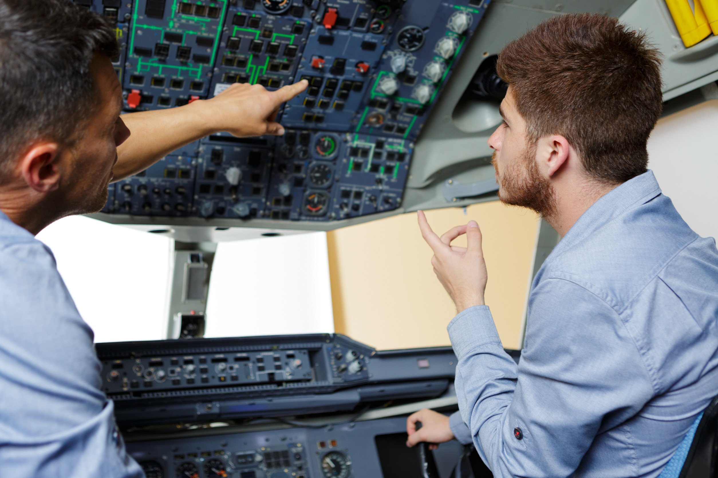flight instructor pointing and explaining the various controls inside of an airplace cockpit to his aviation student