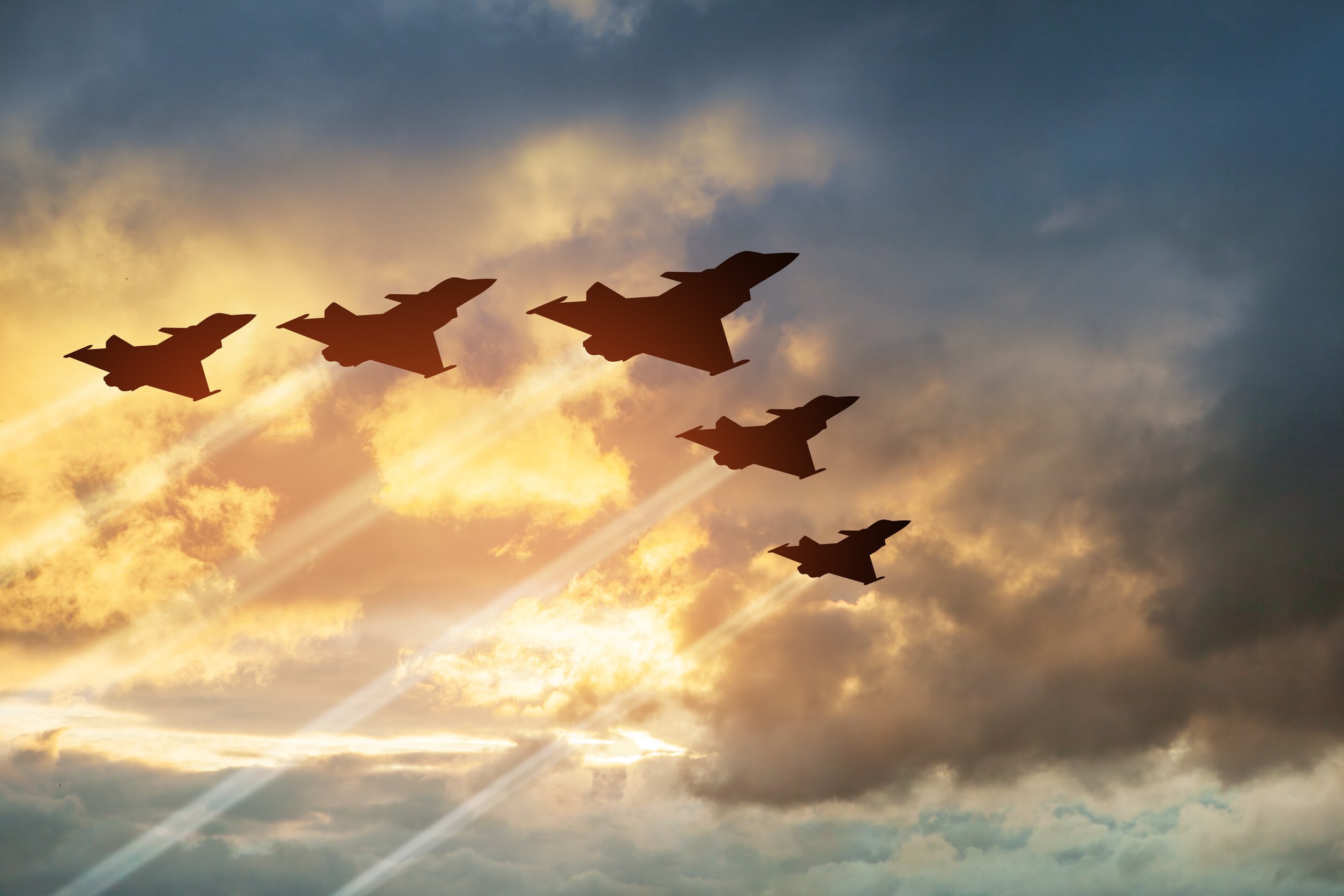 silhouette of air force fighter jets flying in formation against the backdrop of a cloudy sky at sunset