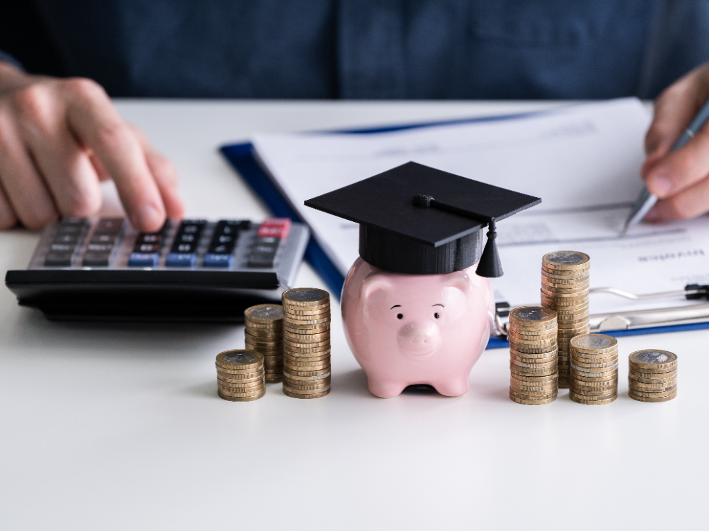 close-up of piggy bank wearing graduation hat and stacked coins in front of businessperson