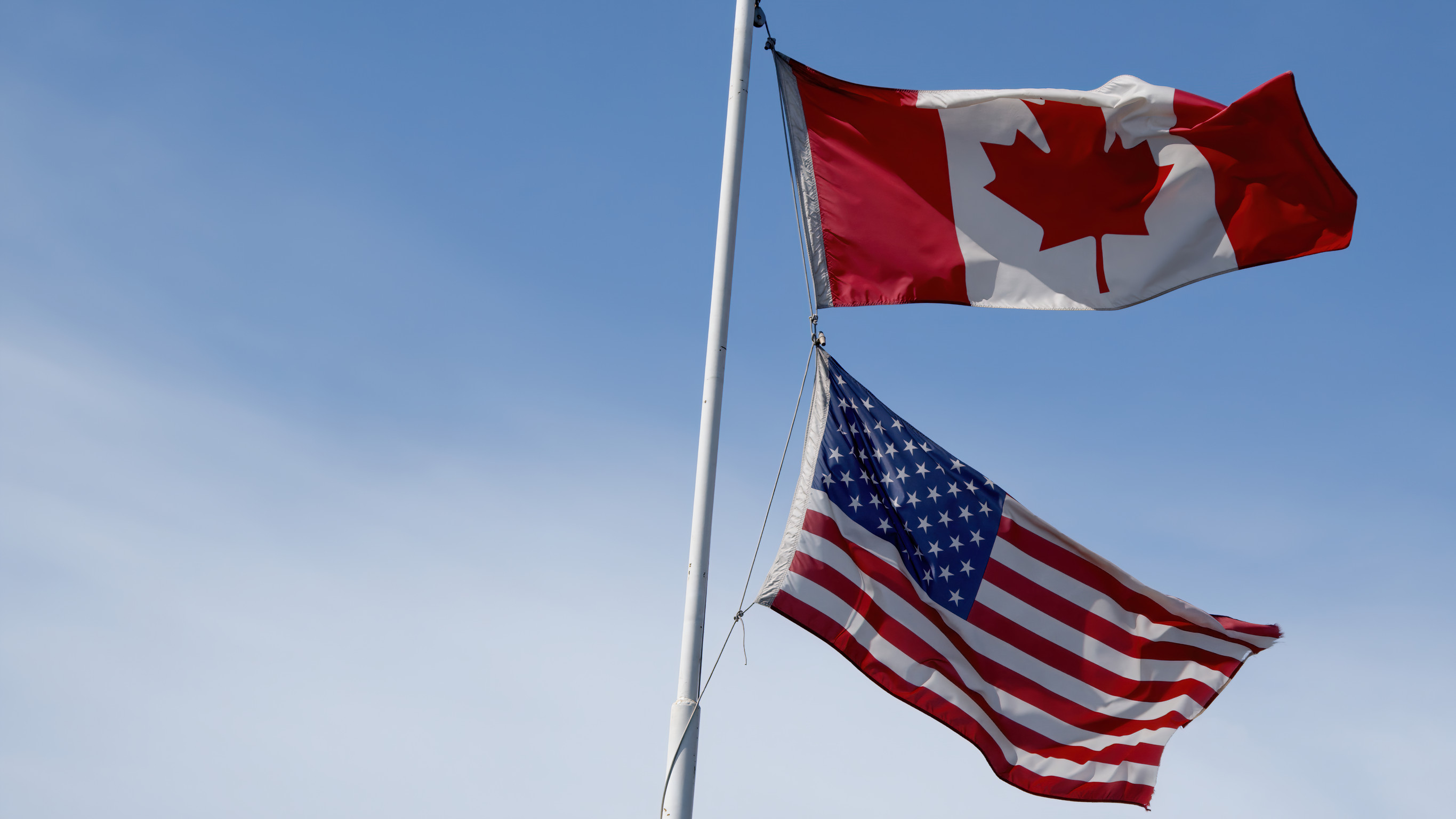 the american and canadian flags fly together on the same flag pole