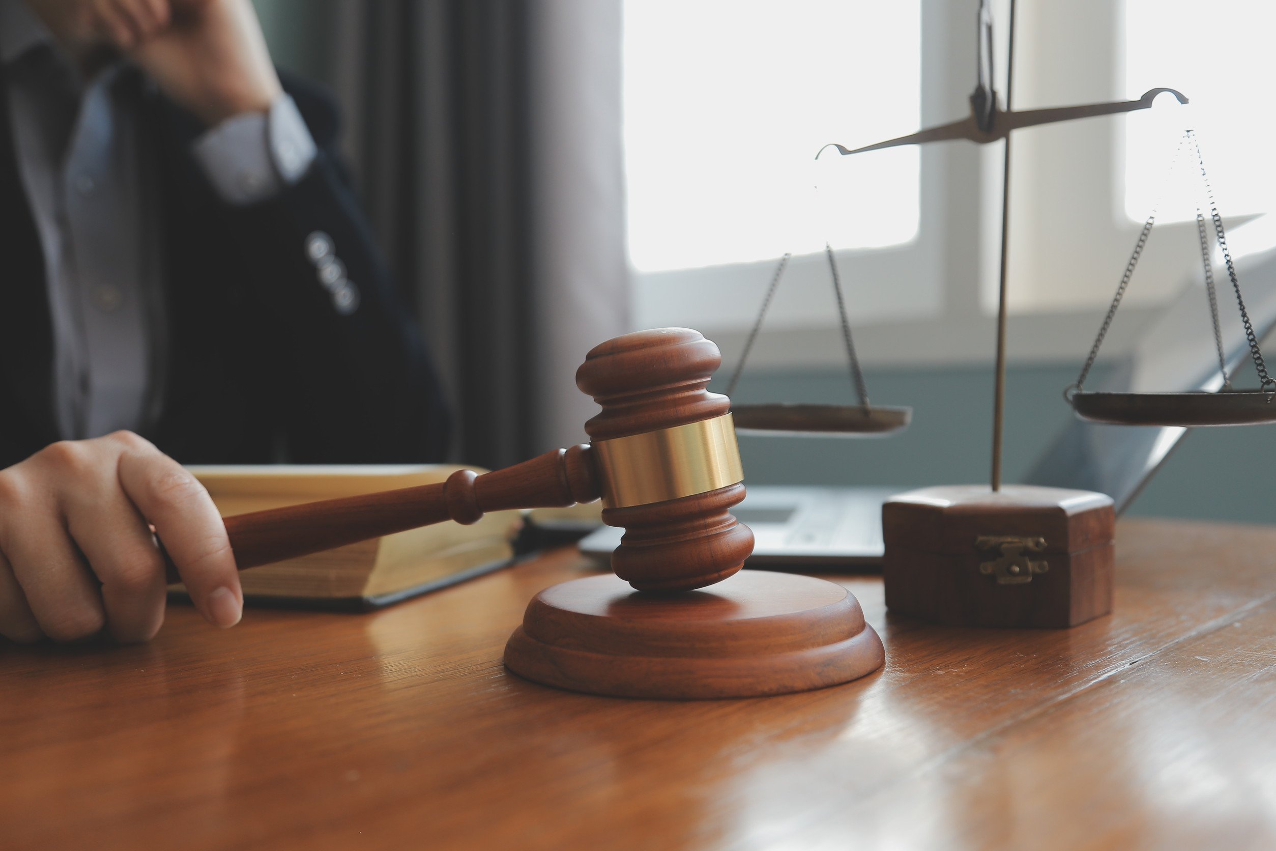 person sitting at a desk with a judge's gavel in hand and a law book opened in front of them