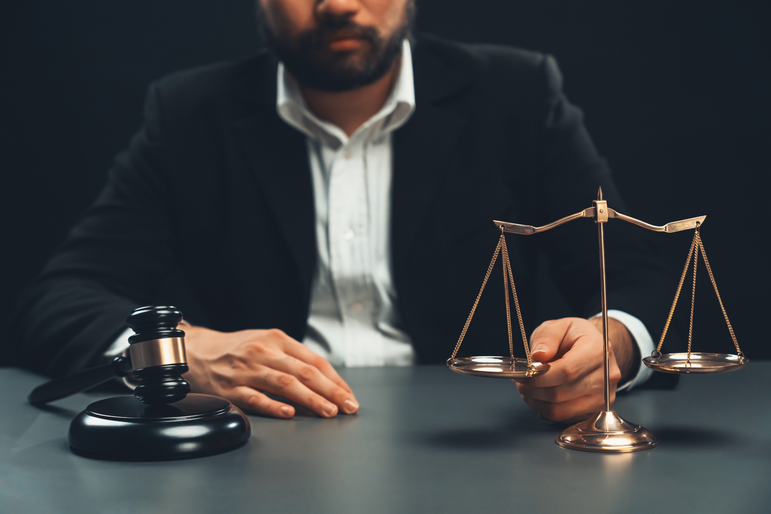 man at a desk looking at a gavel and the scales of justice. 