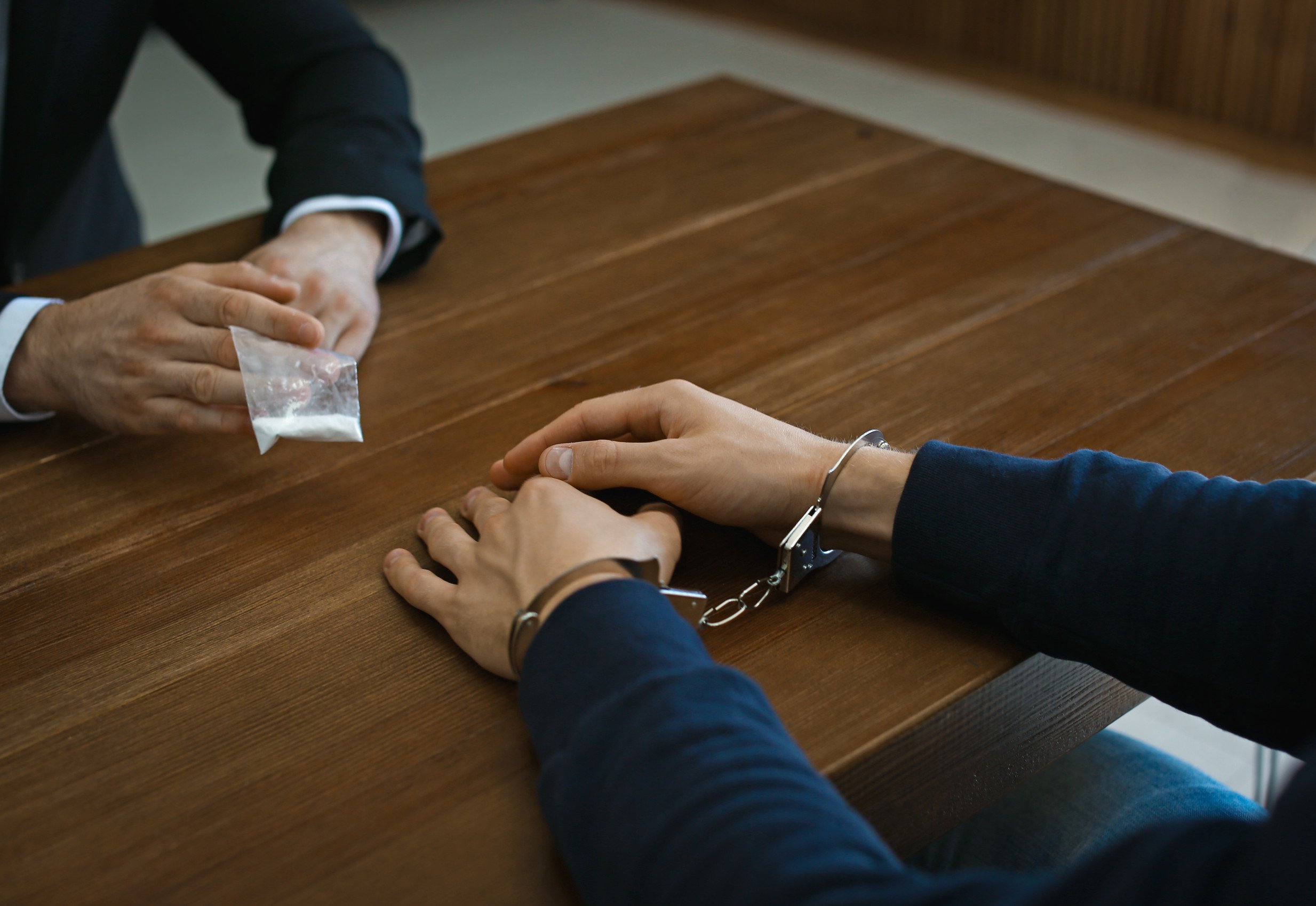DEA agent interrogating alleged drug dealer in handcuffs at desk indoors