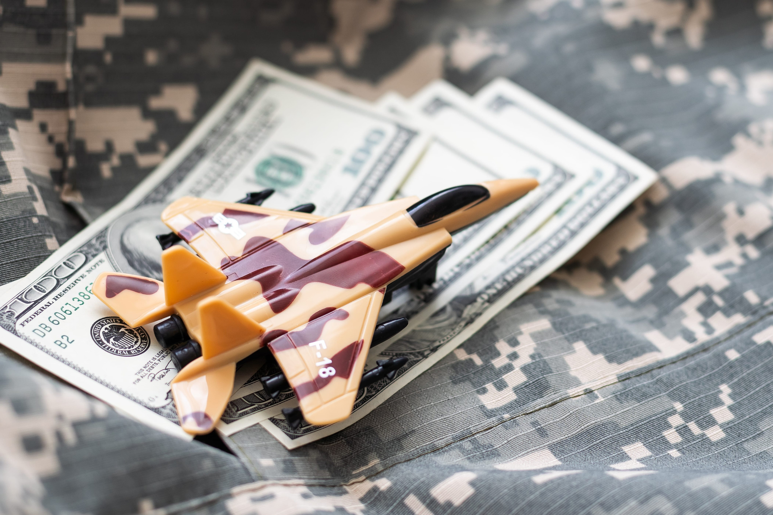 a model military jet rests atop a stack of $100 bills