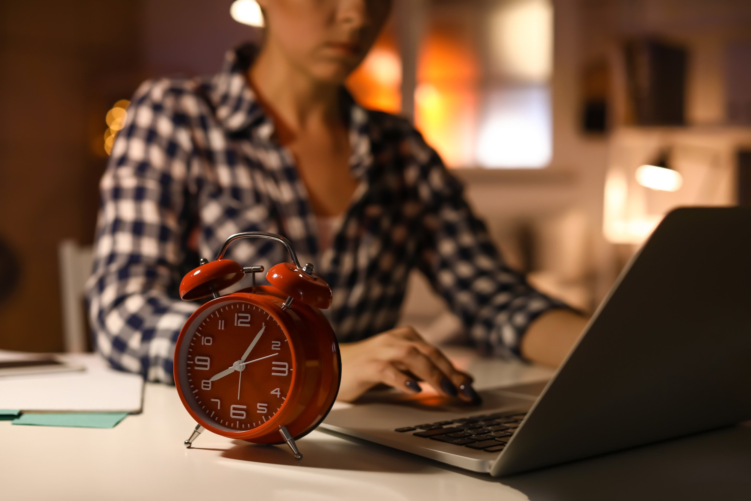 woman working on a laptop with an alarm clock on the desk next to her