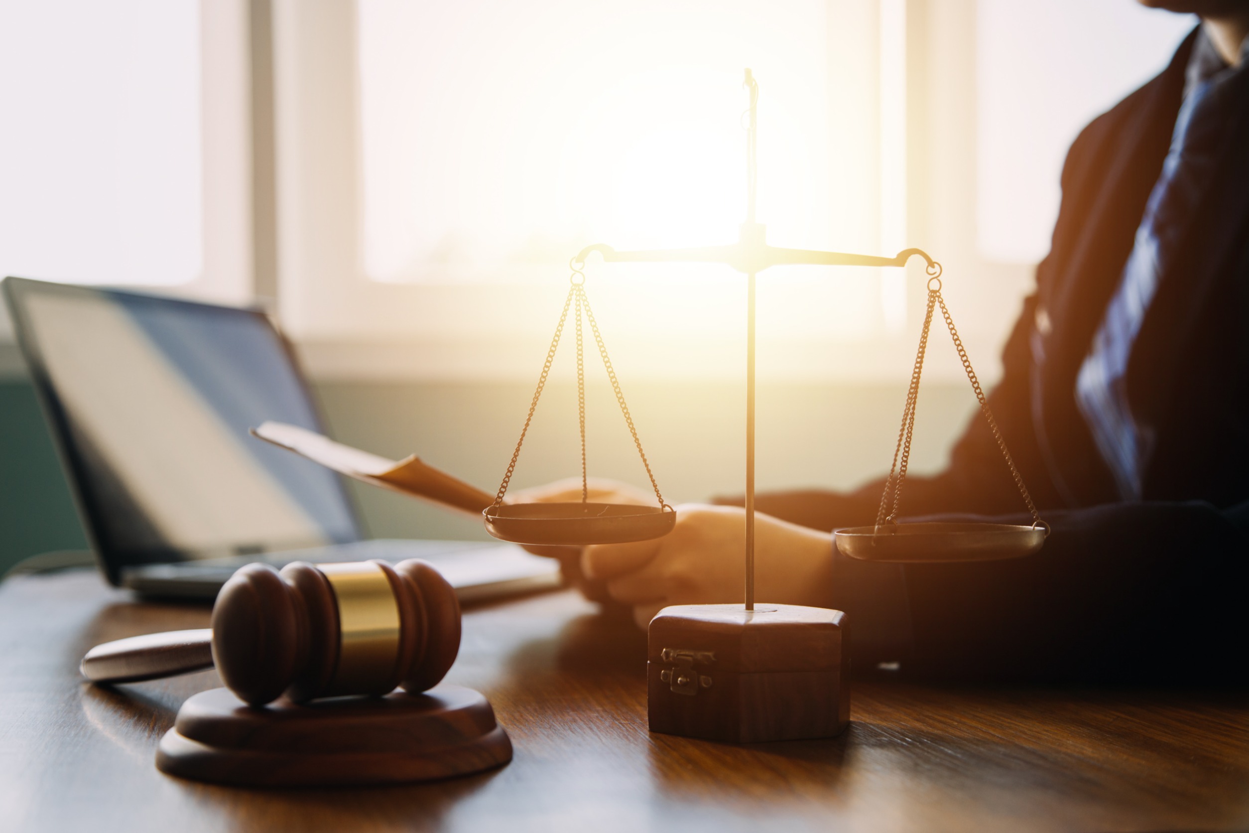 a photo of a person sitting at a desk. On the desk there is a gavel and the scales of justice. 