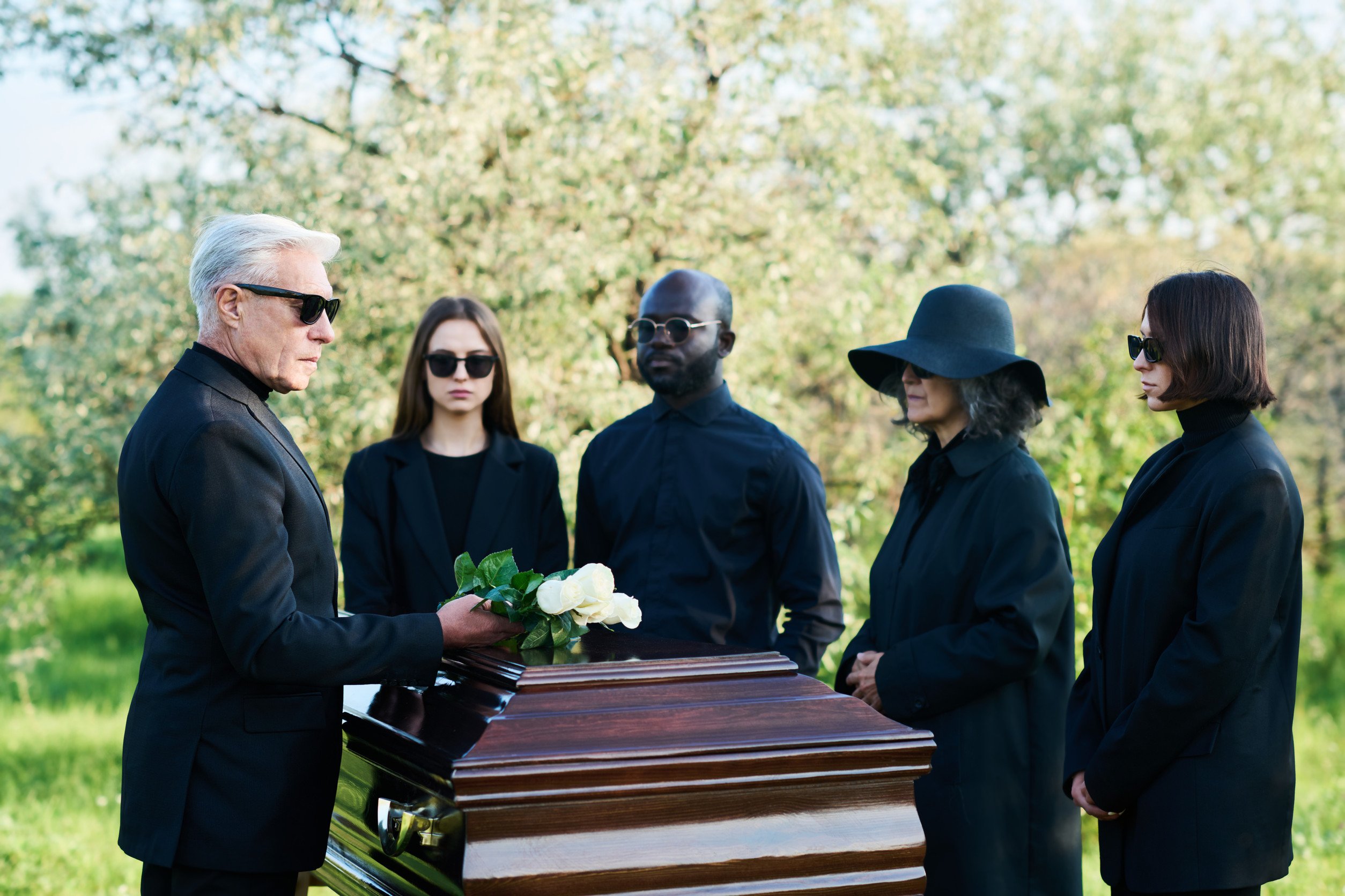 funeral-goers dressed in black standing around a casket outside