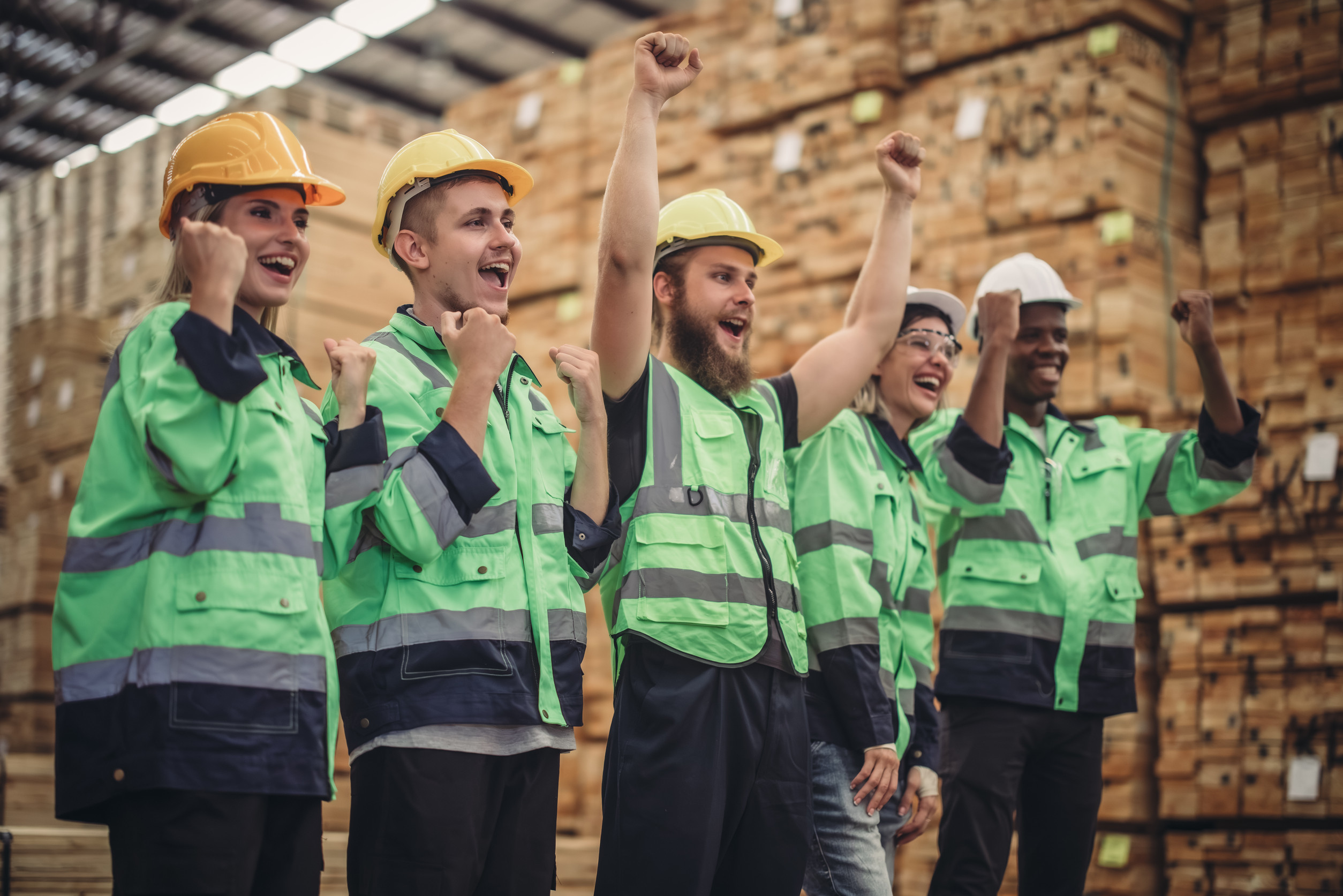 workers in hard hats and visibility vests cheering together in a lumber yard