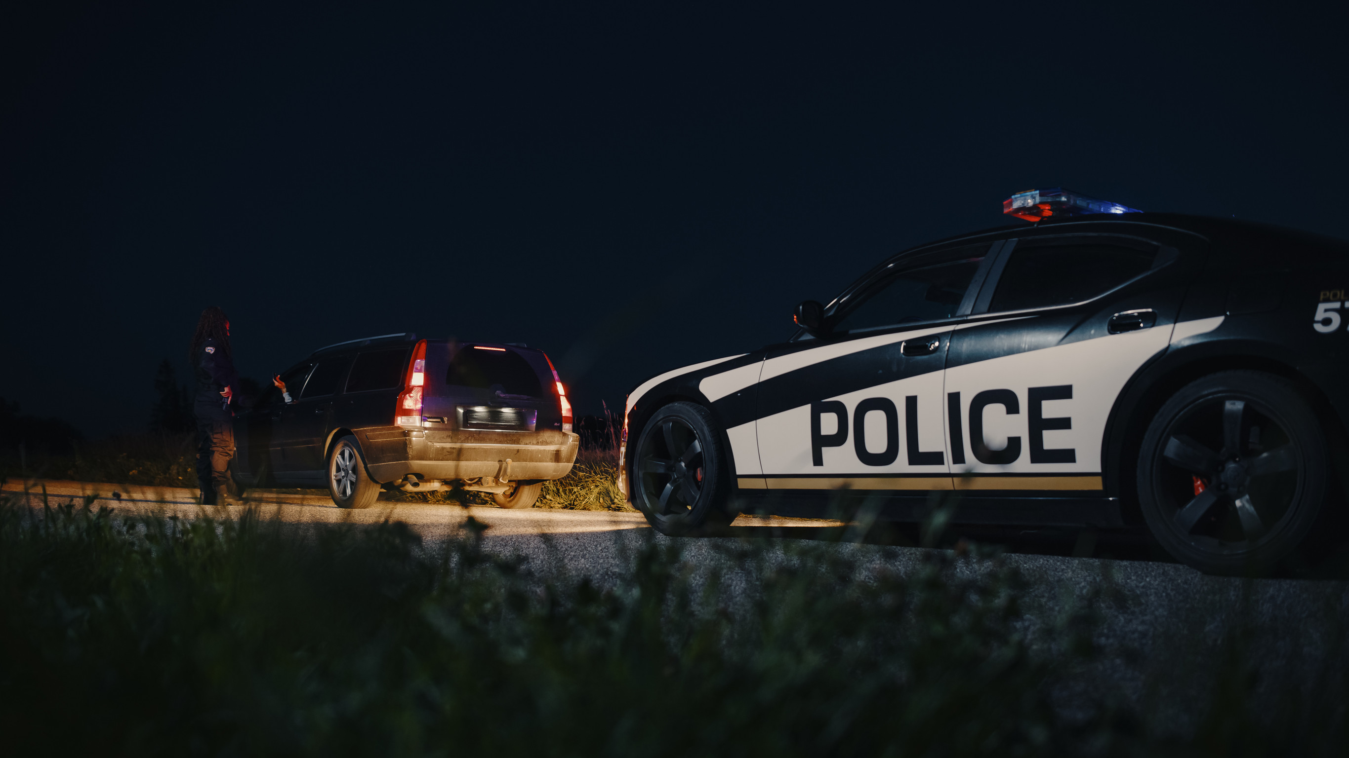 police car pulls over a civilian station wagon at the side of the road at night