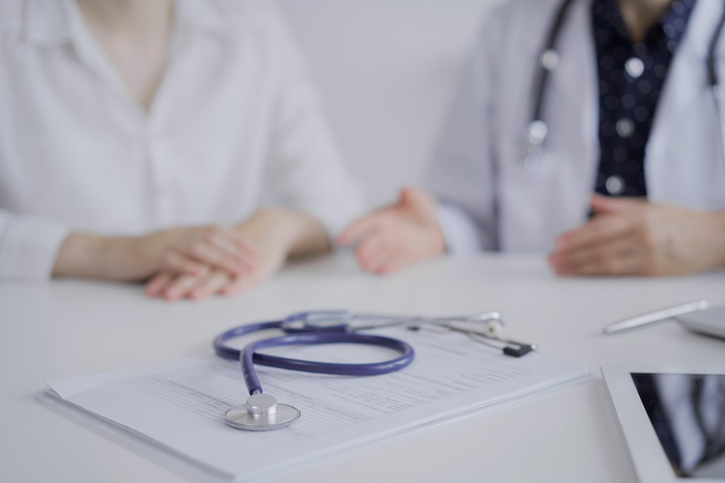 Stethoscope in focus while doctor and a patient gesturing with their hands during a consultation in the clinic