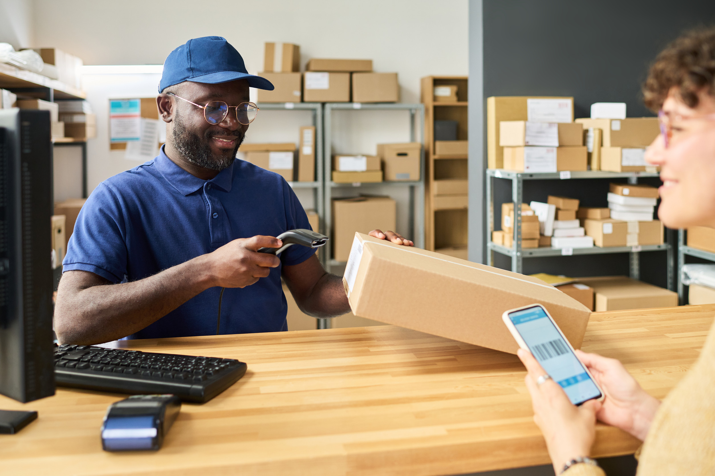 a postal service worker helps a woman with a package at the service counter, scanning in her parcel for delivery