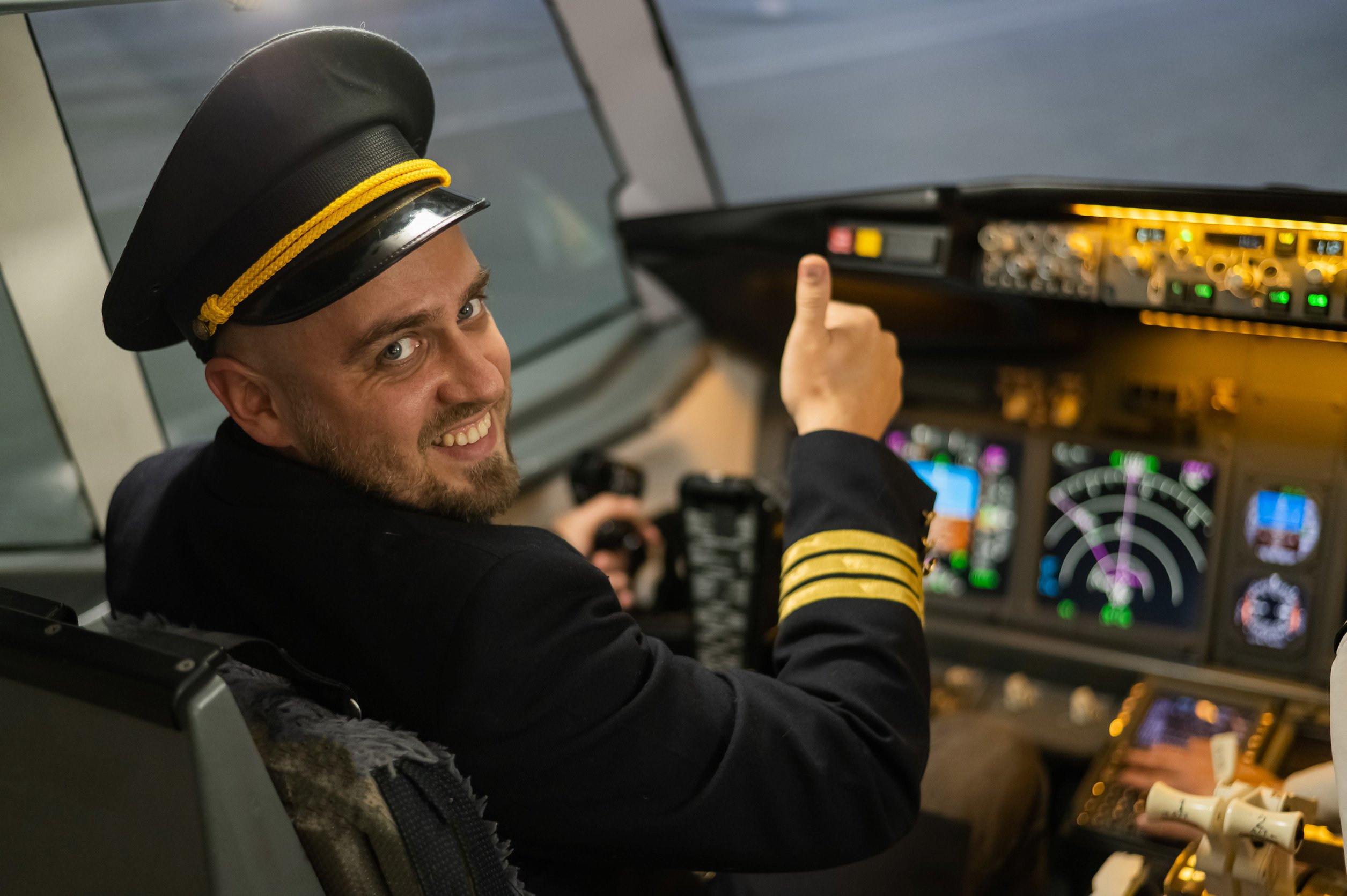 a smiling pilot gives his thumbs up to the camera, looking back from his seat in the cockpit