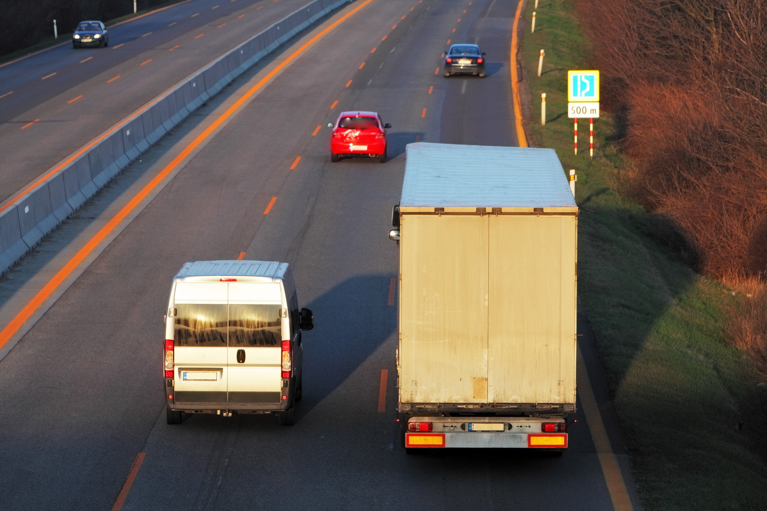 a box truck cruises alongside a van and a few other cars down a highway
