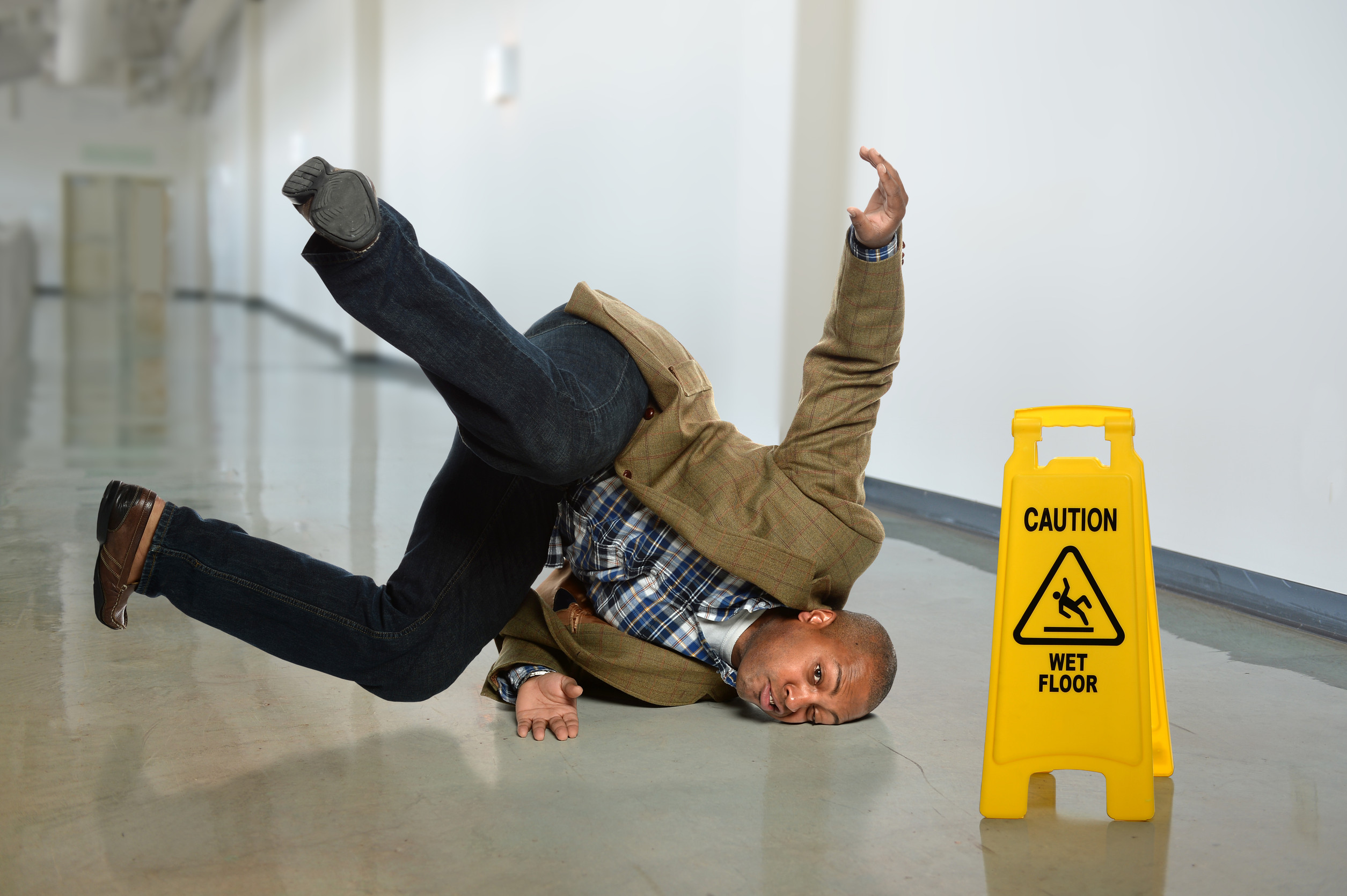 cool guy slips and falls by a wet floor sign in an office setting
