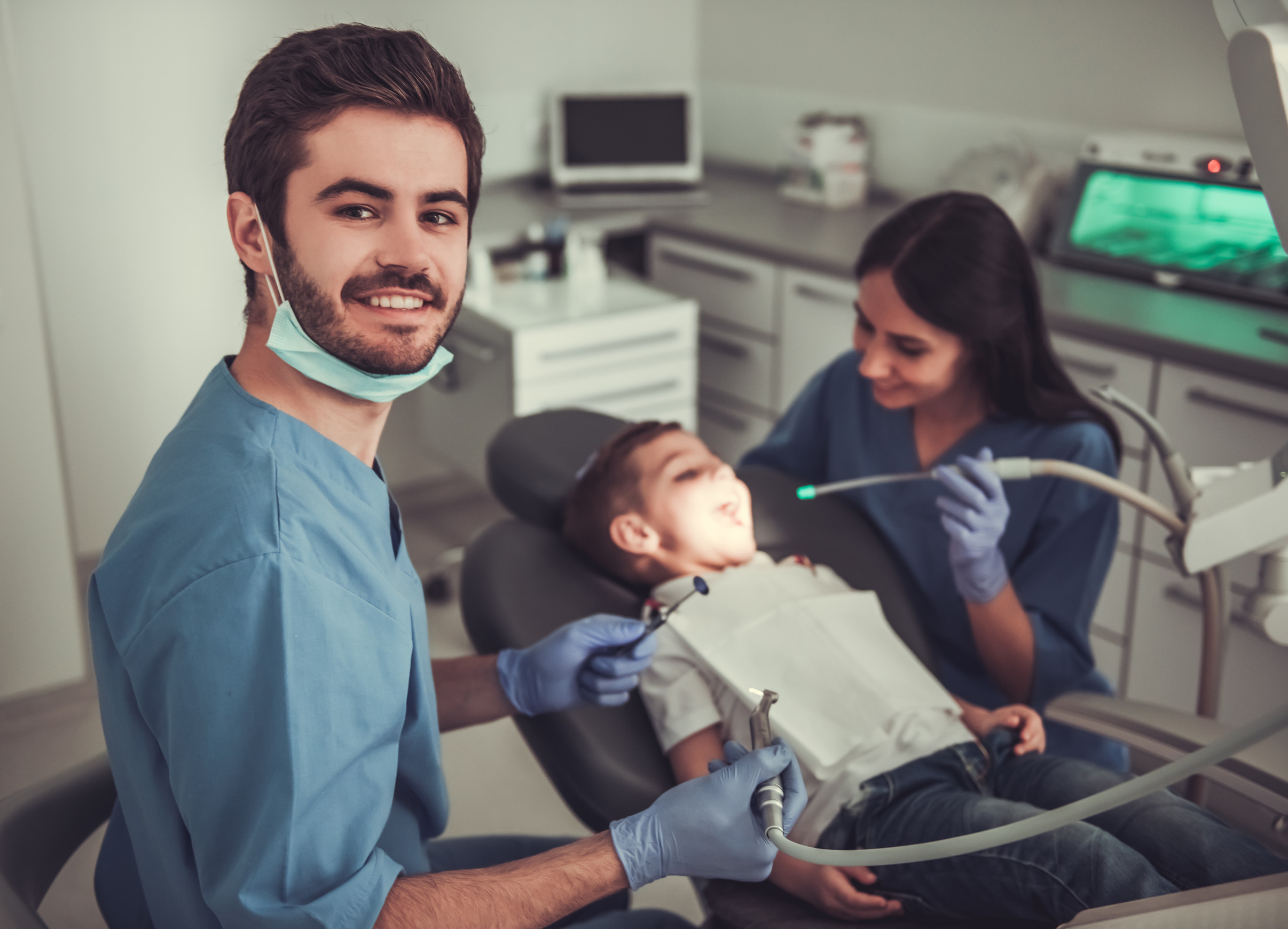 a dentist and their assistant work on the teeth of a small child in a dentist's chair