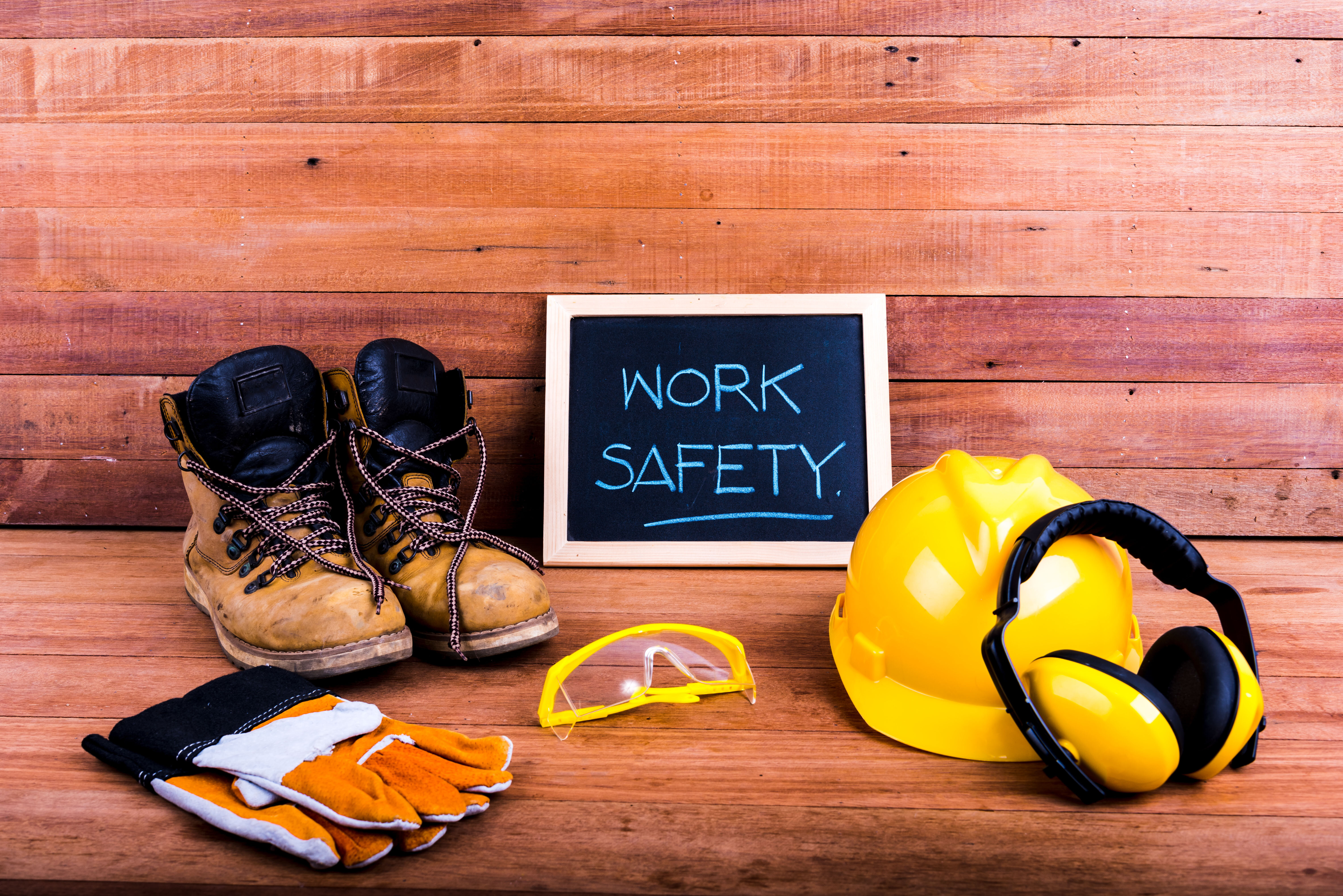 Safety gear and chalkboard with text WORK SAFETY on wooden background