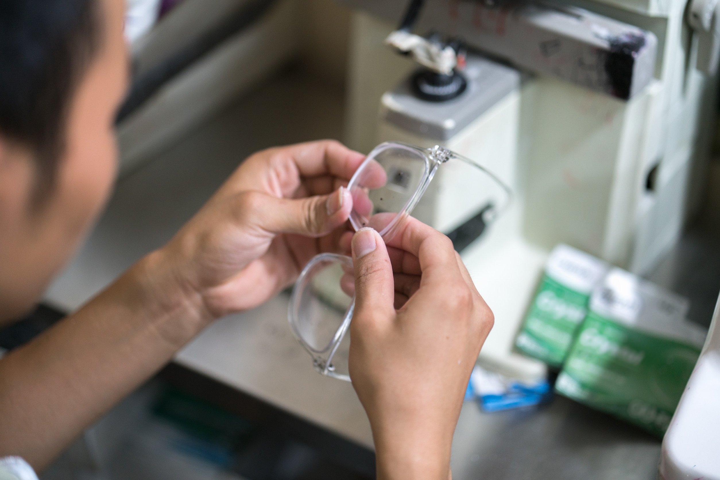 a technician inspects and adjusts glasses by hand in a lab in front of a machine