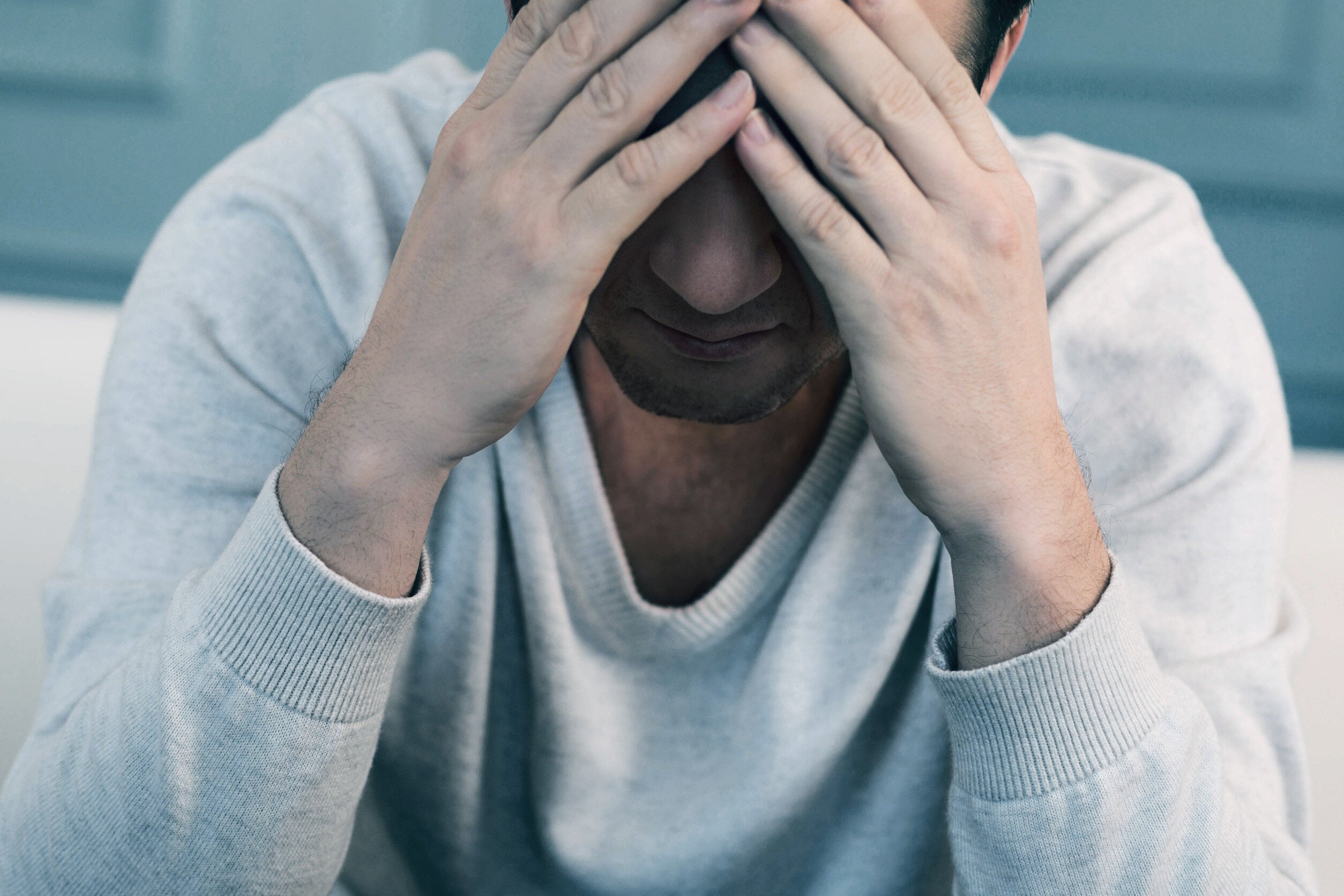 a distressed man holds his head in his hands with a weary demeanor