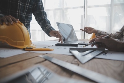 Construction businessmen having a conversation over a desk that has a laptop and tools.